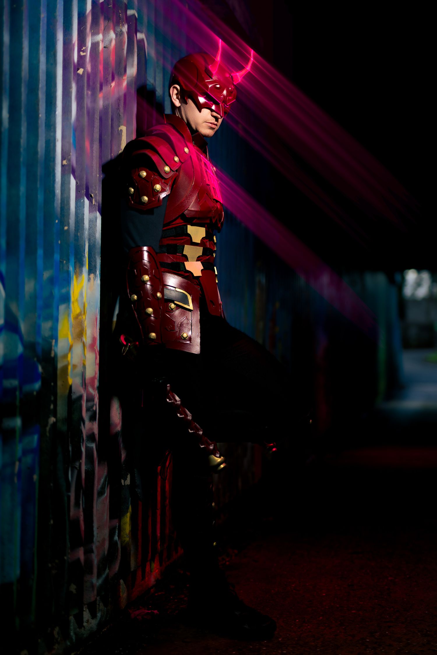 Cosplayer in Marvel Rival Daredevil armour and horned helmet leans on a graffiti wall, magenta light streaks cutting through the dark.