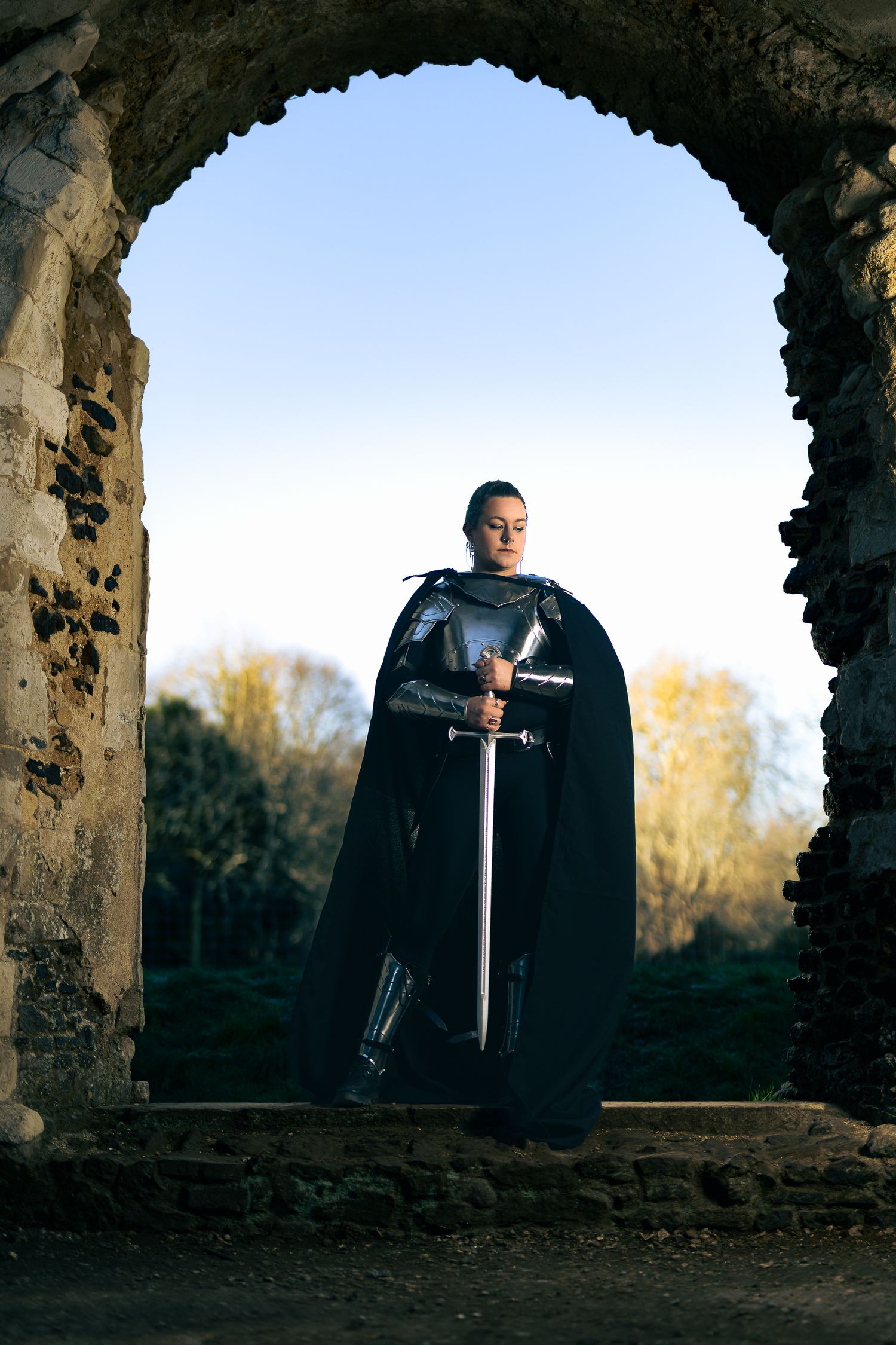 Dramatic medieval-style photoshoot with a sword-wielding figure in stone ruins at sunset.