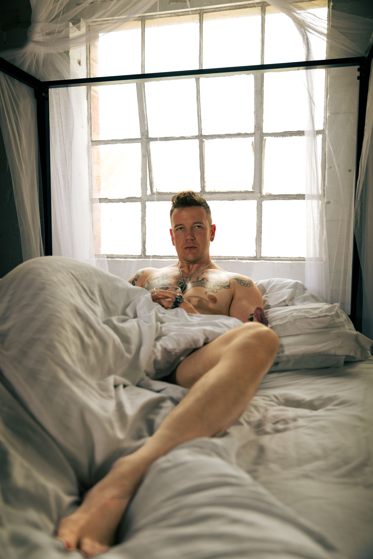 Intimate bedroom photoshoot with natural window lighting and white bedding.