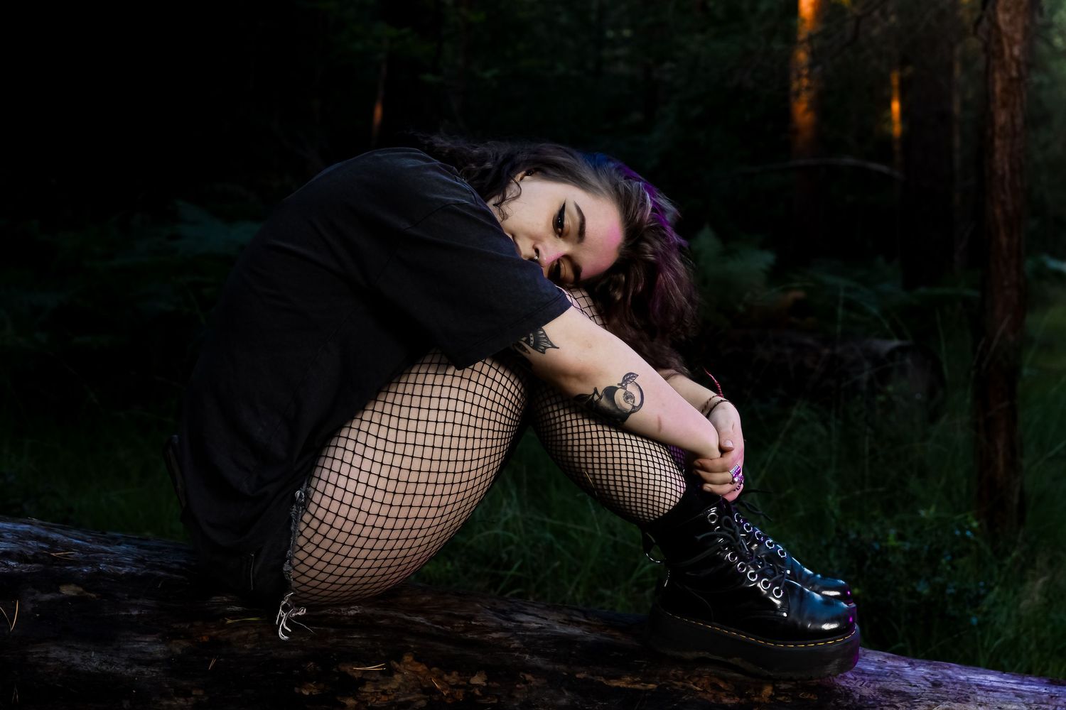 Moody forest scene with figure reclining on mossy ground in dark attire.