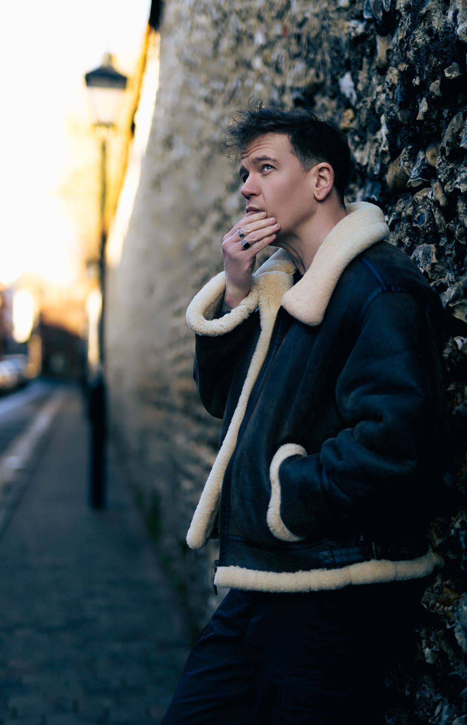 Close portrait of a man leaning against a textured wall, thoughtful expression and soft background blur