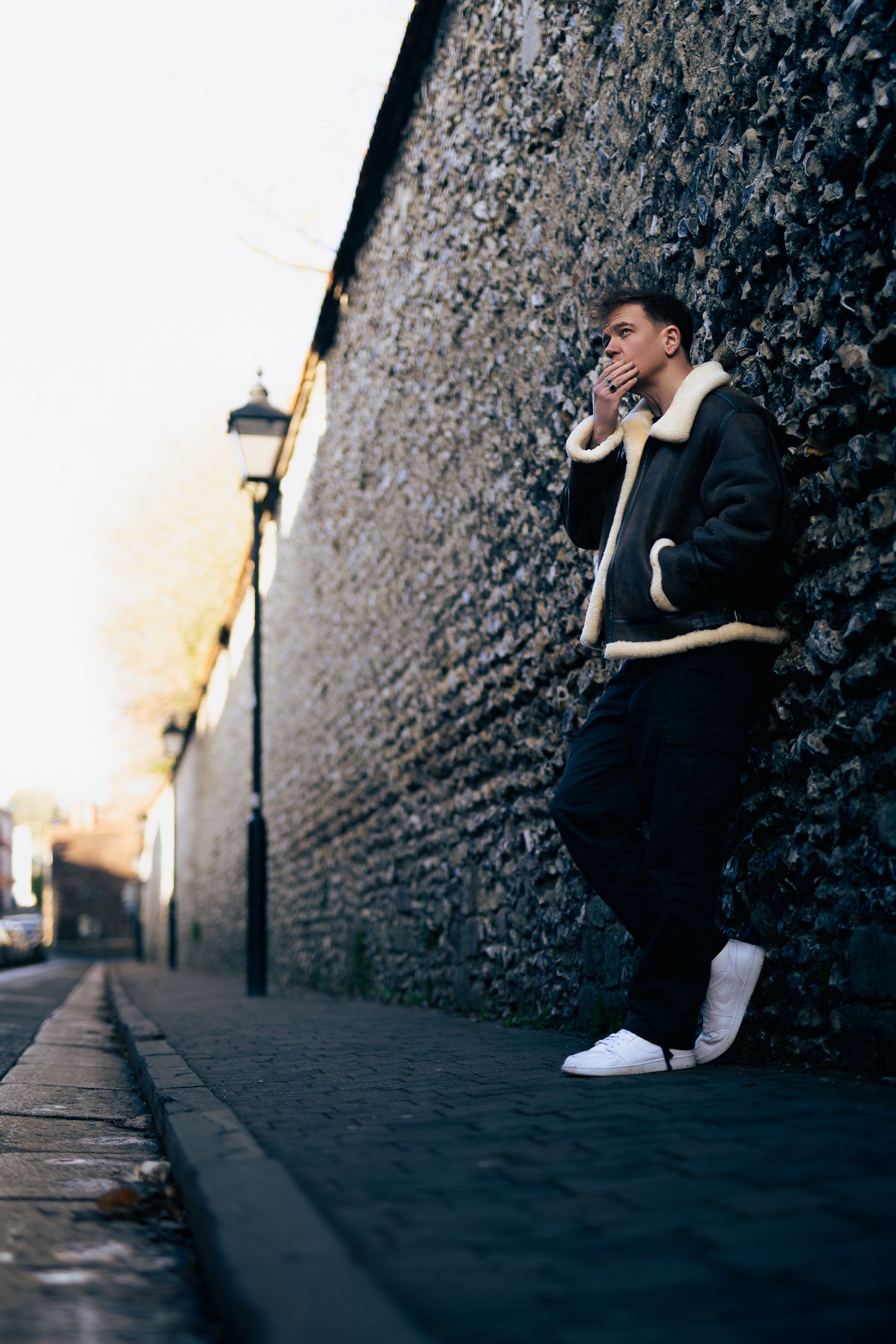 Environmental portrait of a man leaning on a long stone wall, wide composition with depth and leading lines