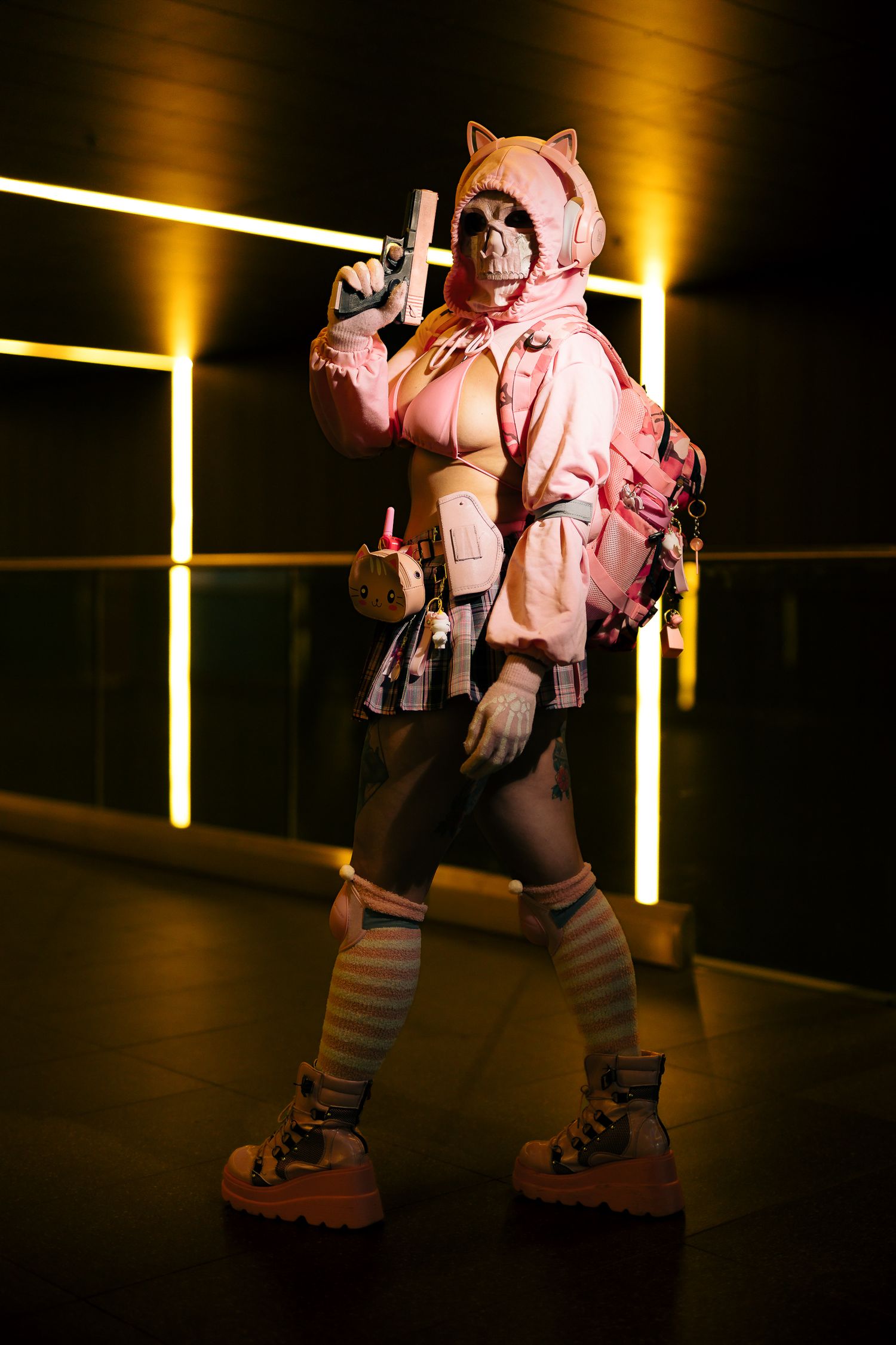 Pink cat hoodie cosplay costume with gas mask, backpack, and prop gun posed in neon-lit corridor.