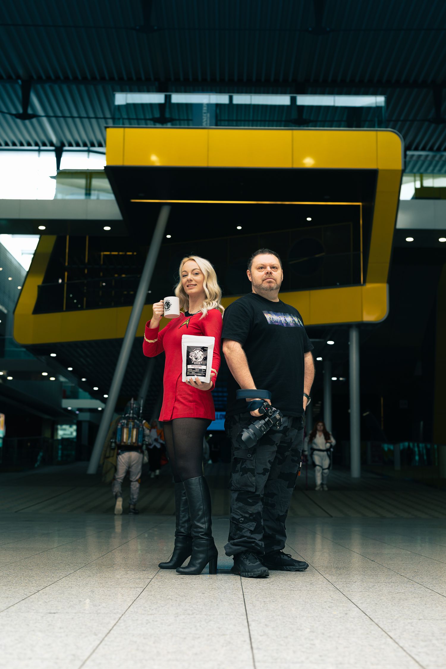 Full-body branding portrait of two people posed in a modern venue interior with bold architectural background
