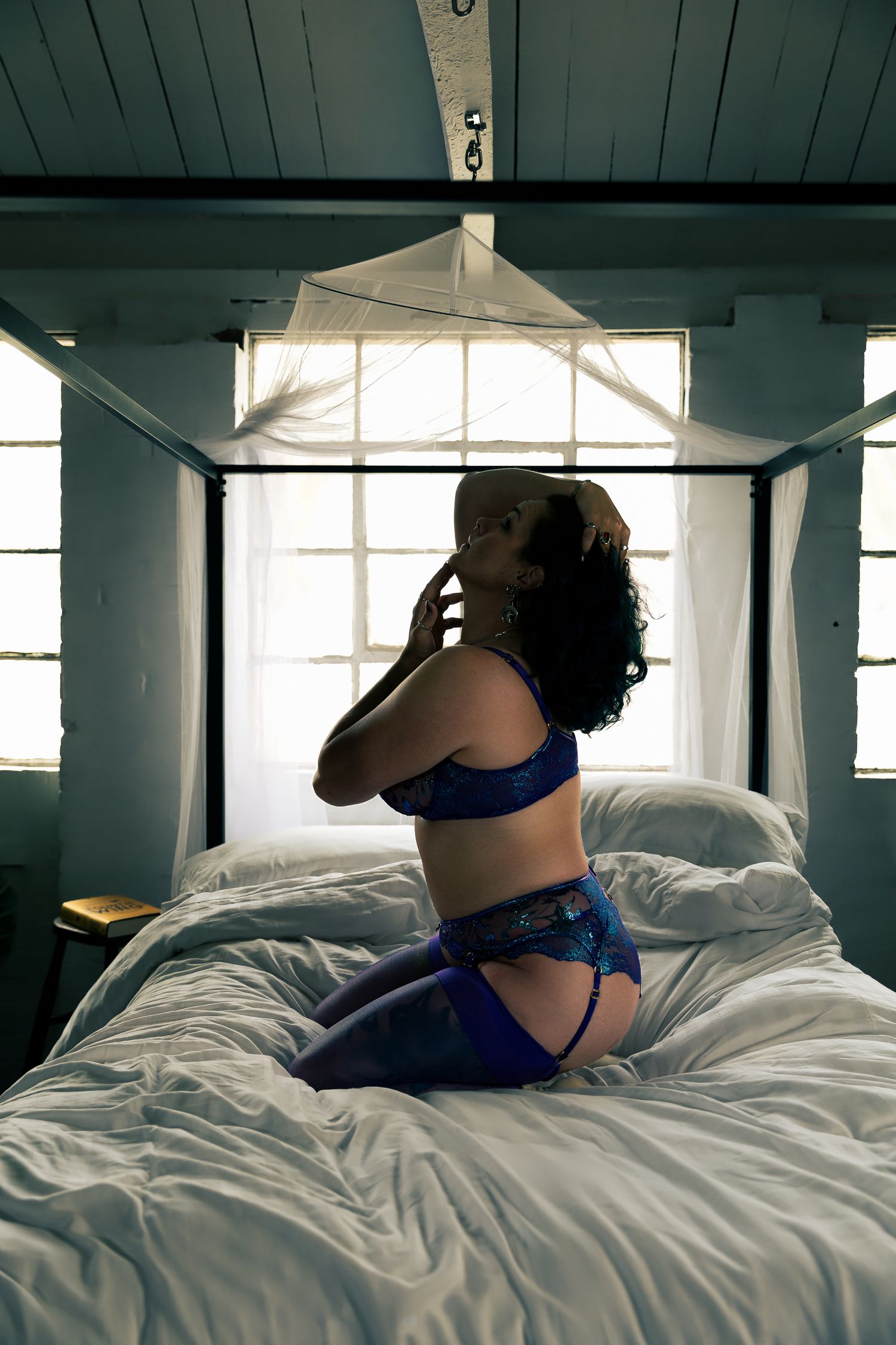 Sensual bedroom scene with blue accents and white bedding in natural window light.