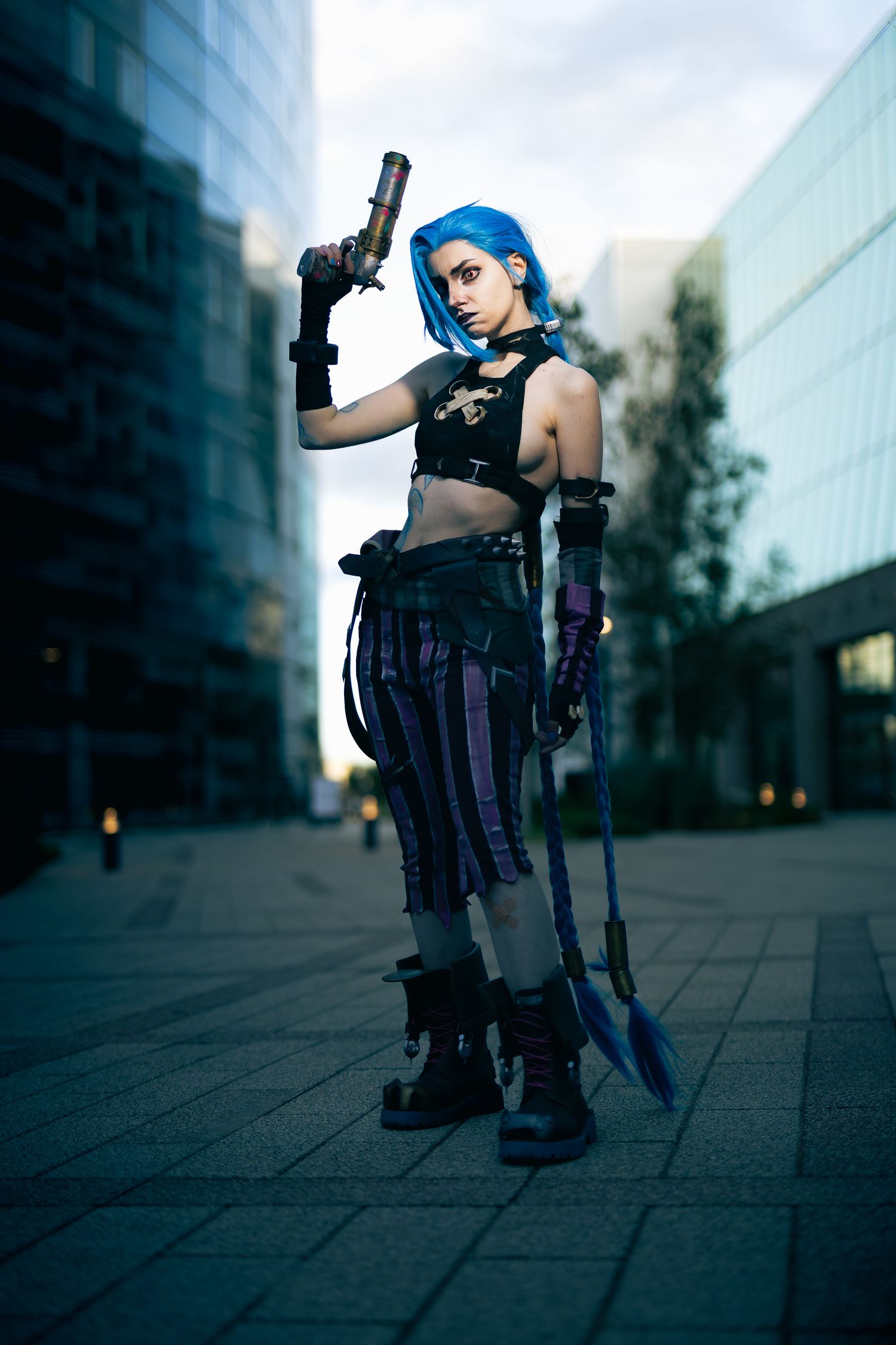 Urban cosplay featuring character with blue hair and tactical gear holding weapon.