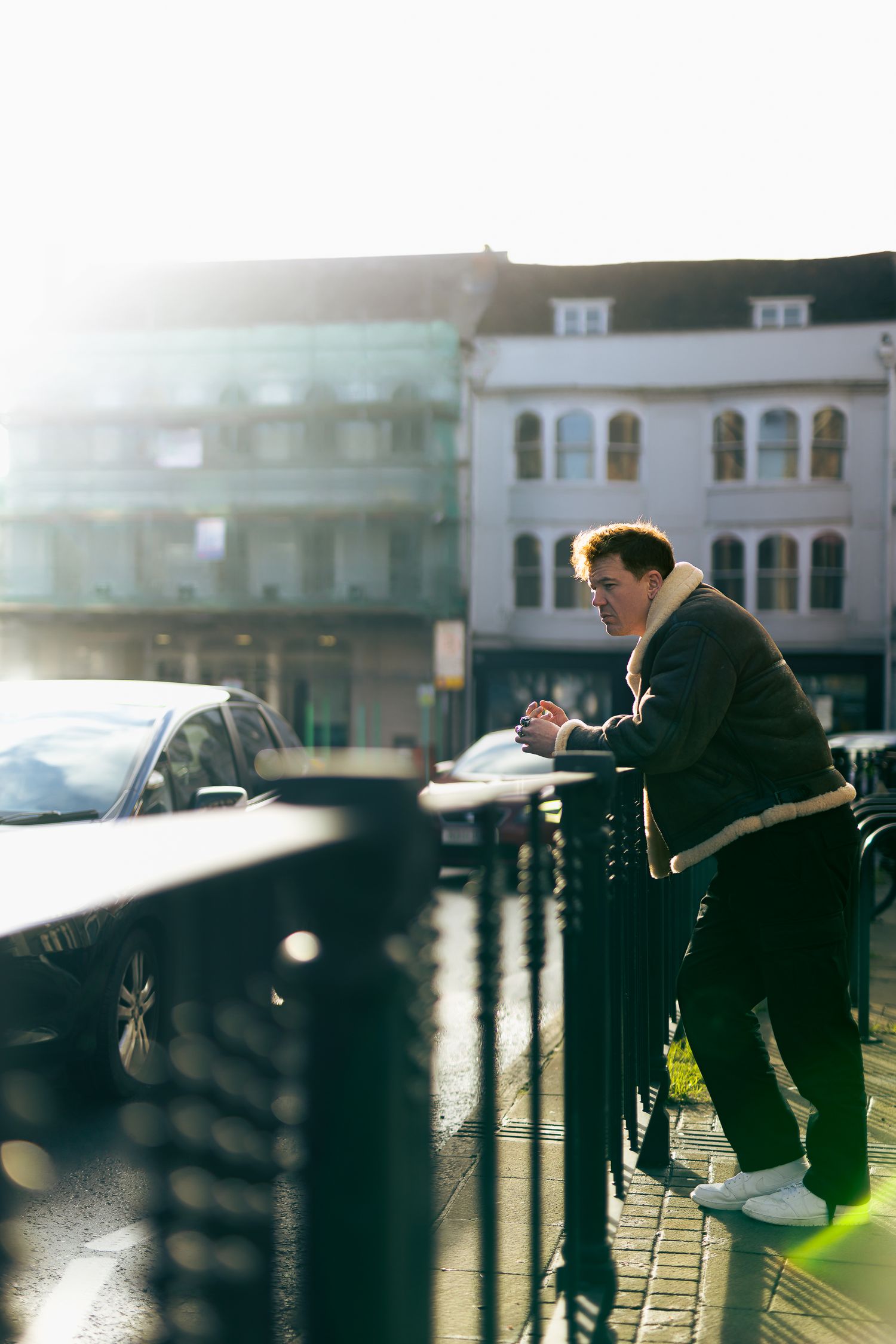 Lifestyle portrait of a man leaning on a railing with sun flare and soft city backdrop