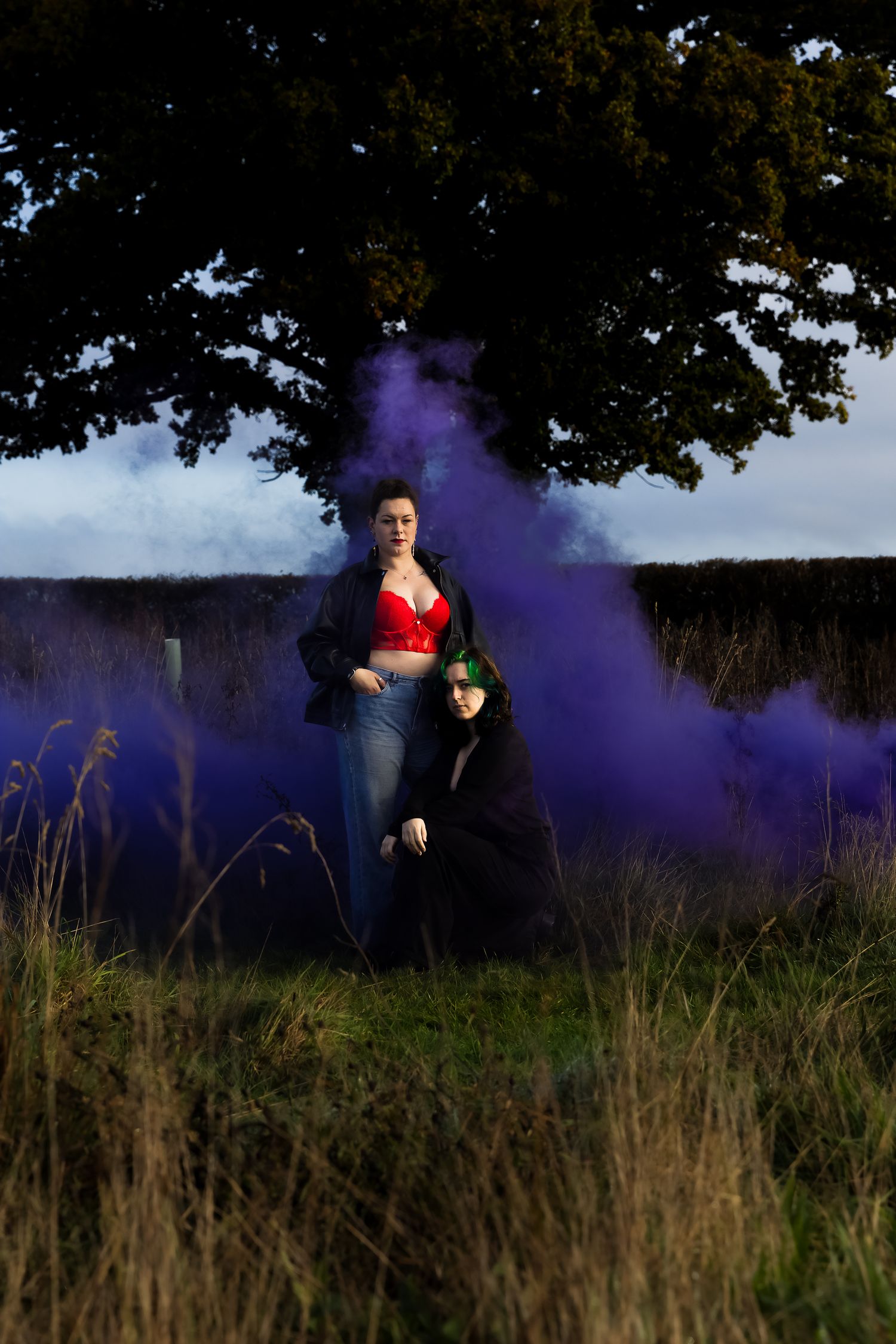 Atmospheric portrait with purple smoke effects in tall grass at sunset.