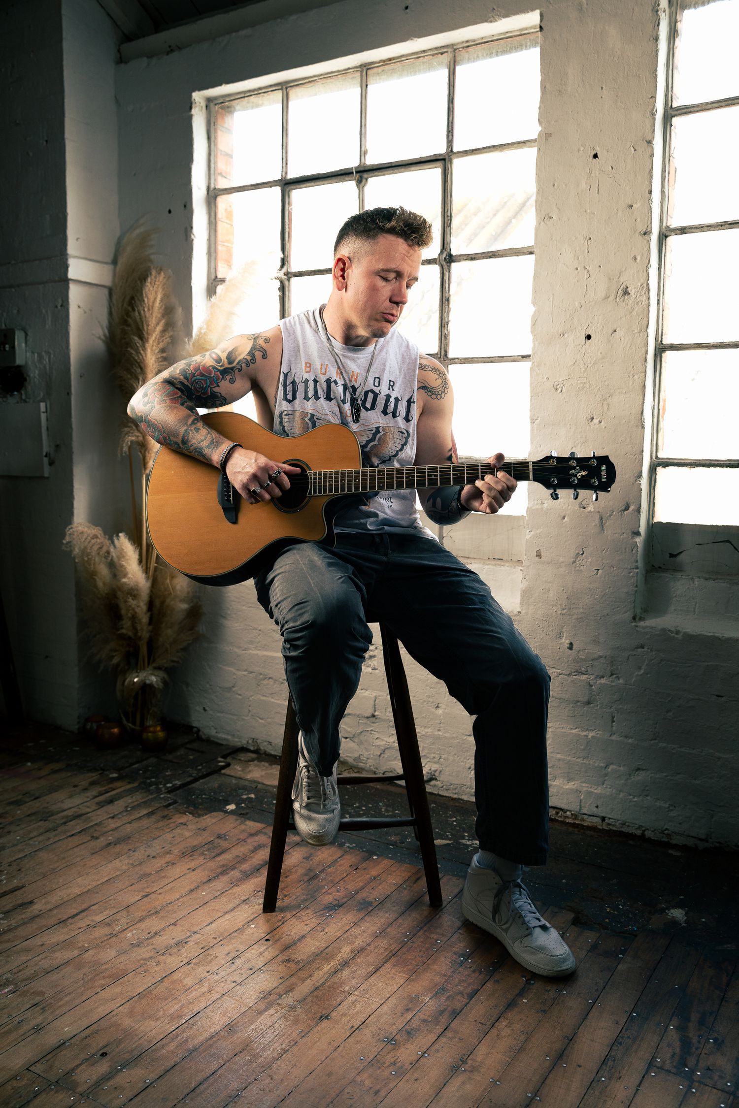 Studio portrait of a musician playing an acoustic guitar by large industrial windows