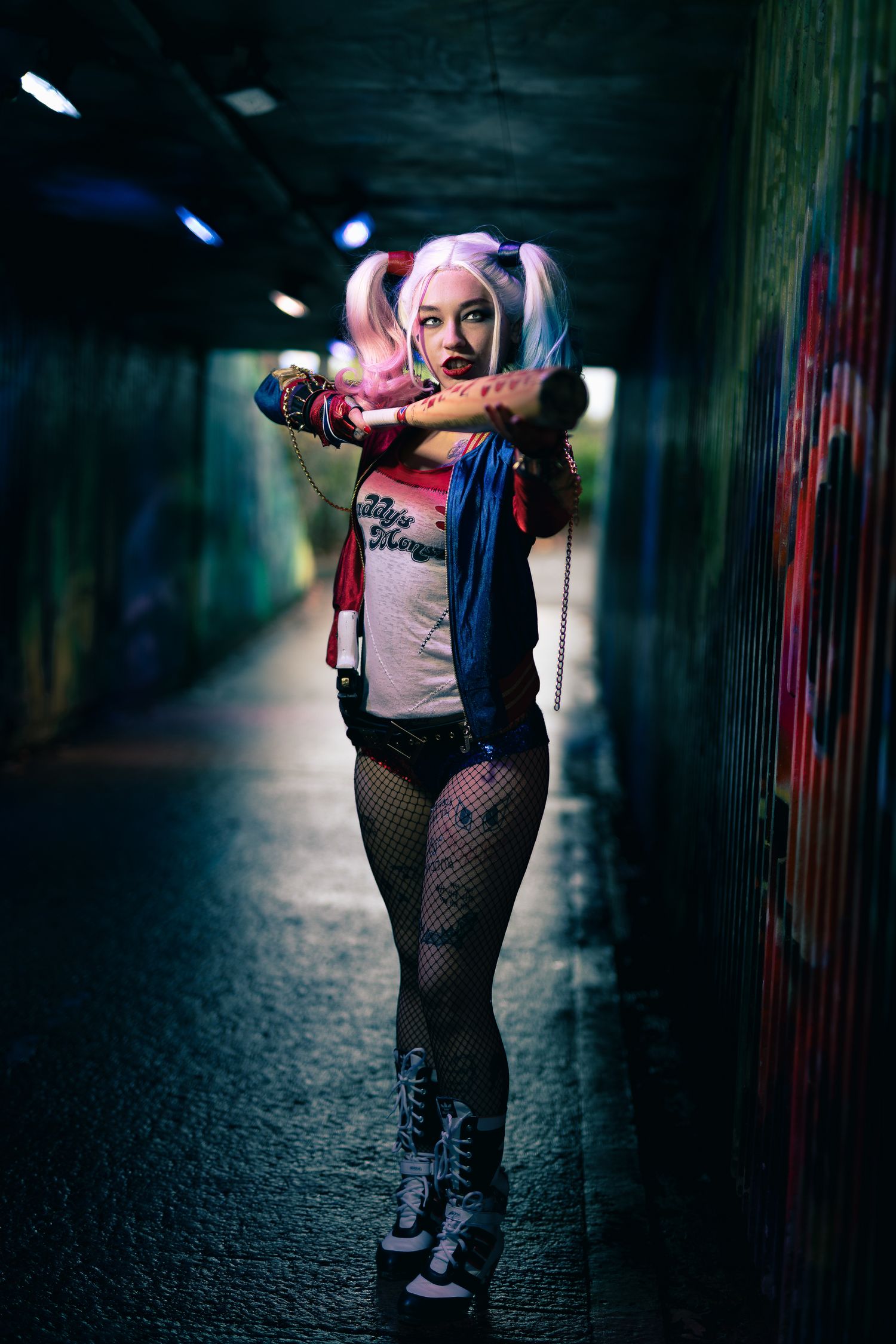 Harley Quinn cosplay aims a baseball bat toward the camera in a graffiti tunnel with cinematic depth of field.