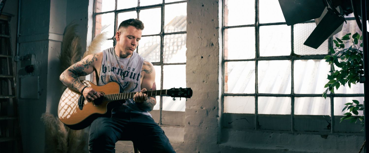 Person playing acoustic guitar in abandoned industrial space with natural lighting.