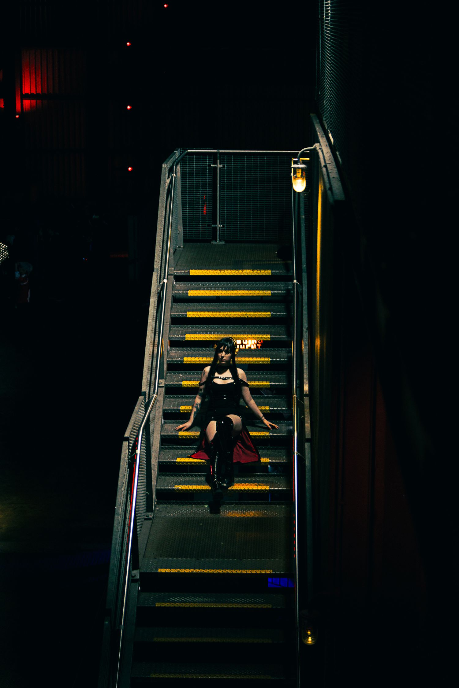 Dramatic photo of cosplayer sitting on illuminated yellow stairs in dark environment.