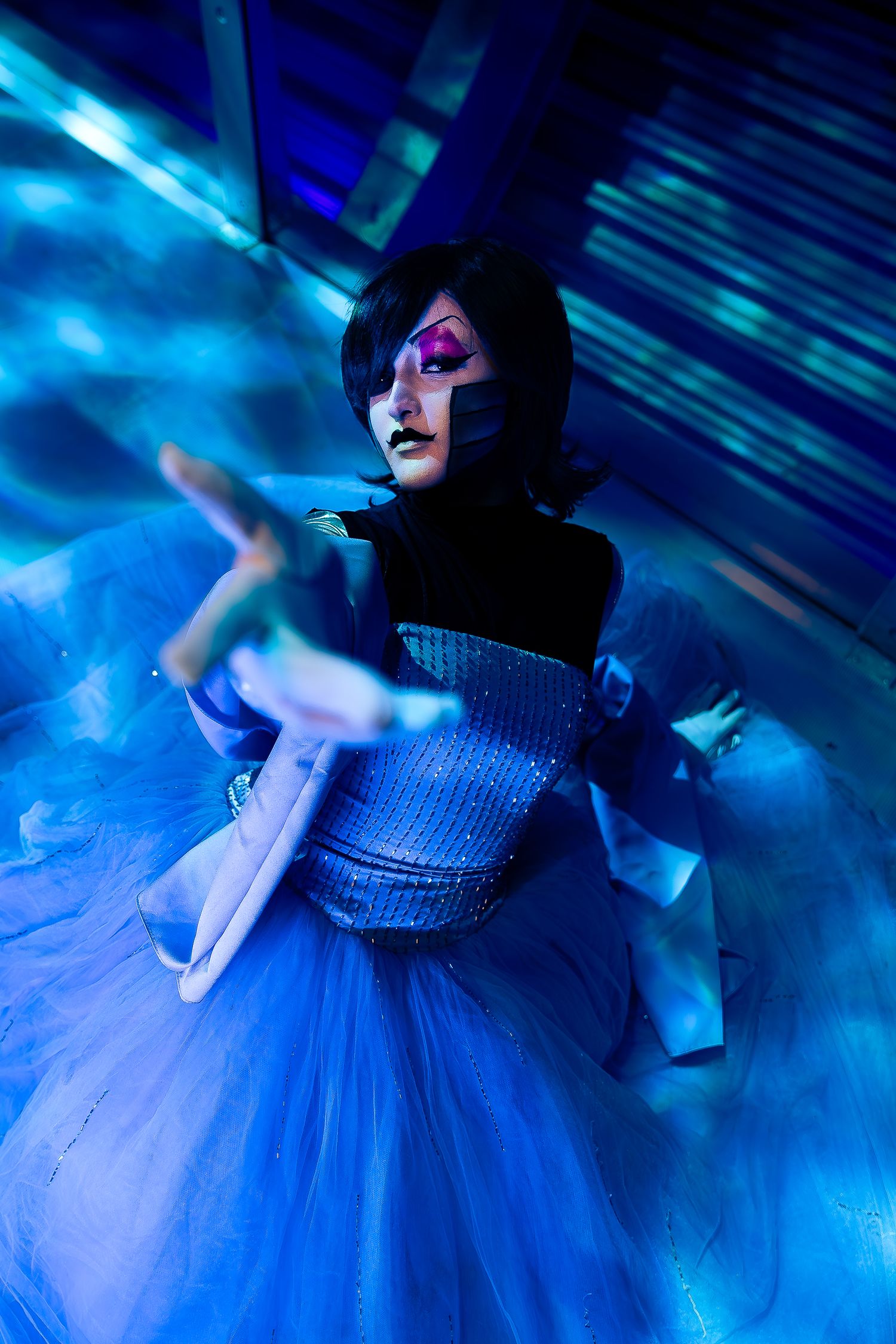 Undertale cosplay with dramatic face paint reaches toward the camera under blue neon lighting.