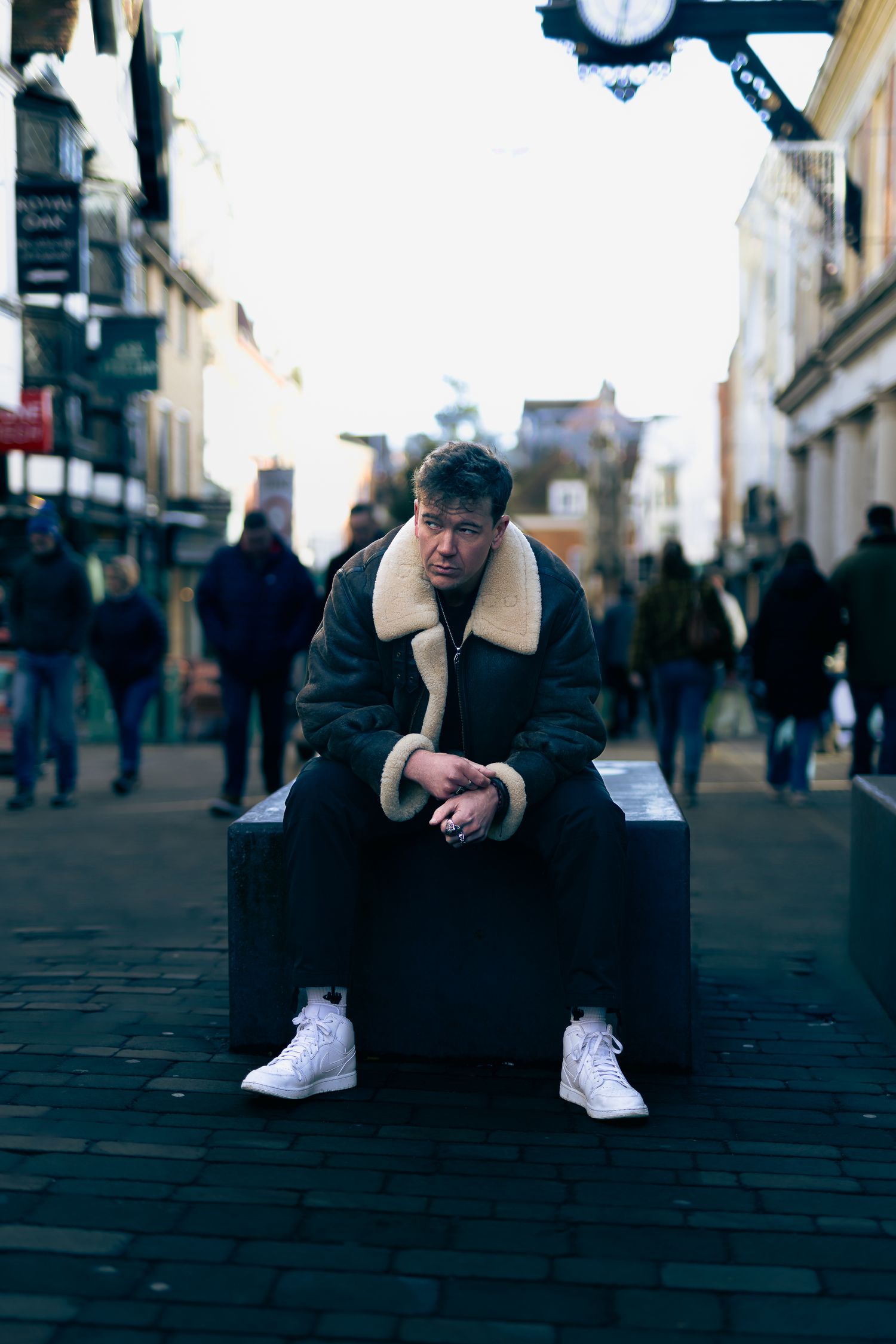 Moody street portrait of a man seated in a busy high street scene, shallow depth of field