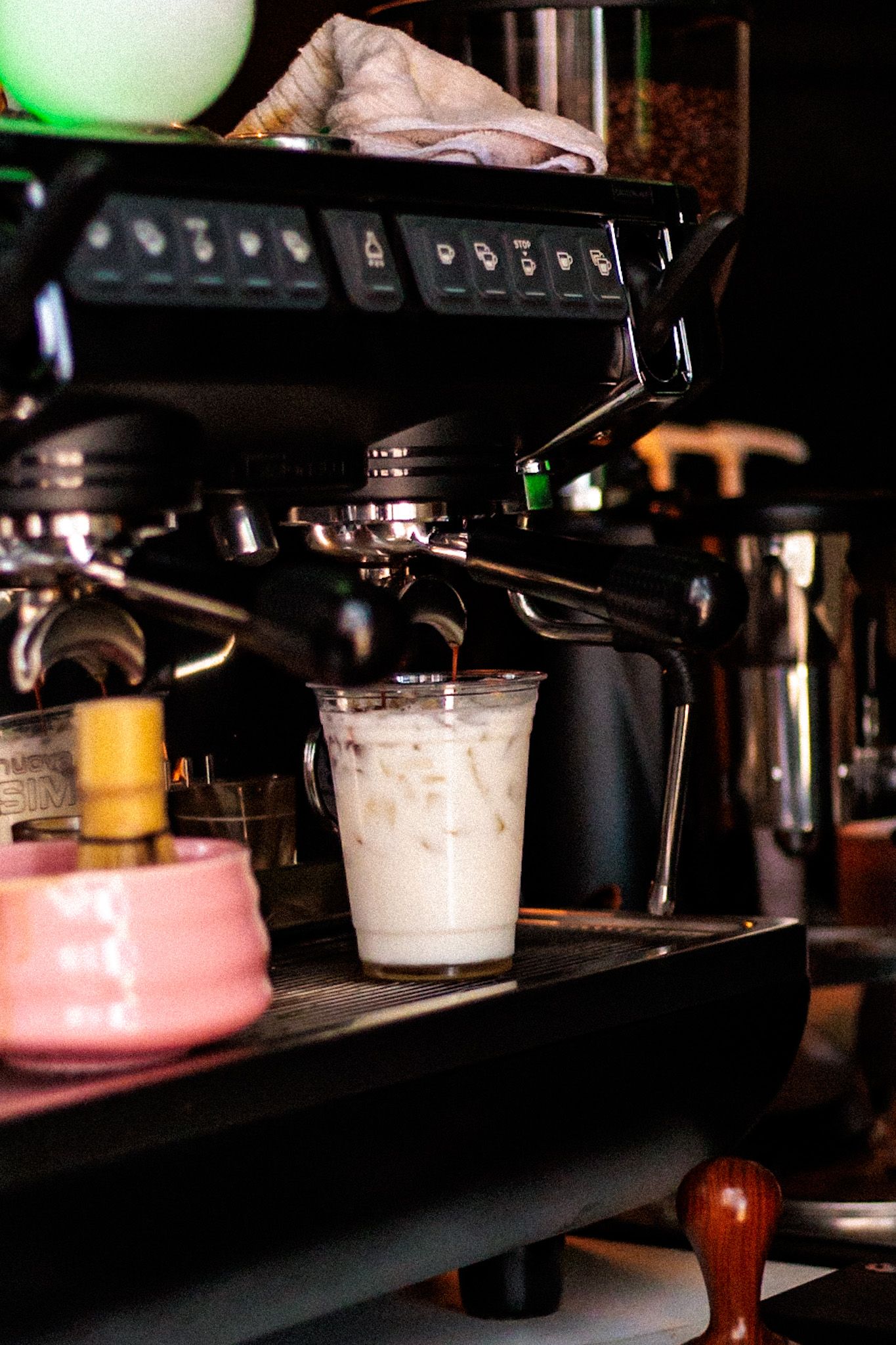 Iced latte in a clear plastic cup being prepared under a professional espresso machine.