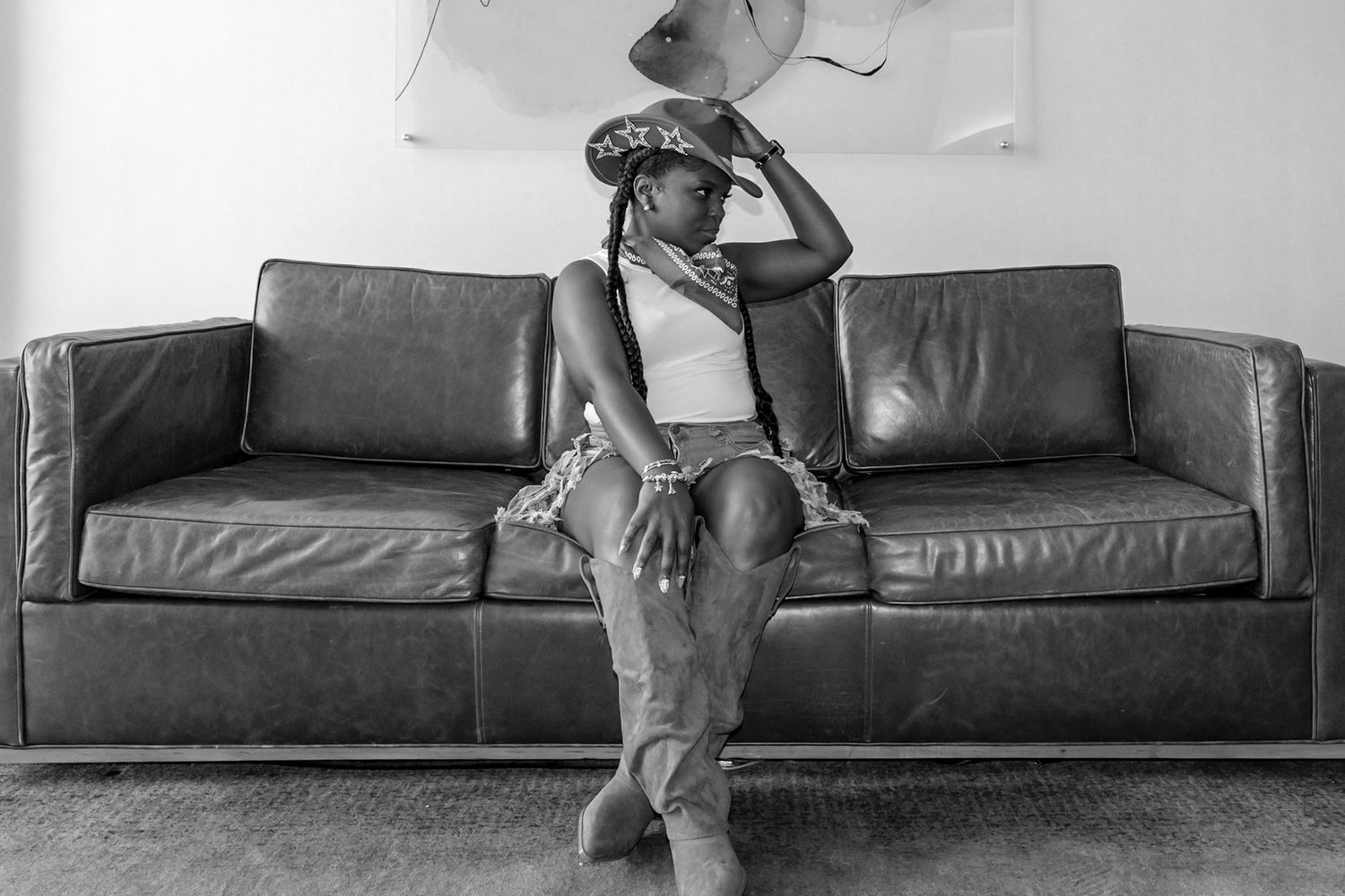 Black and white portrait of woman in hat sitting on leather couch in minimalist interior.