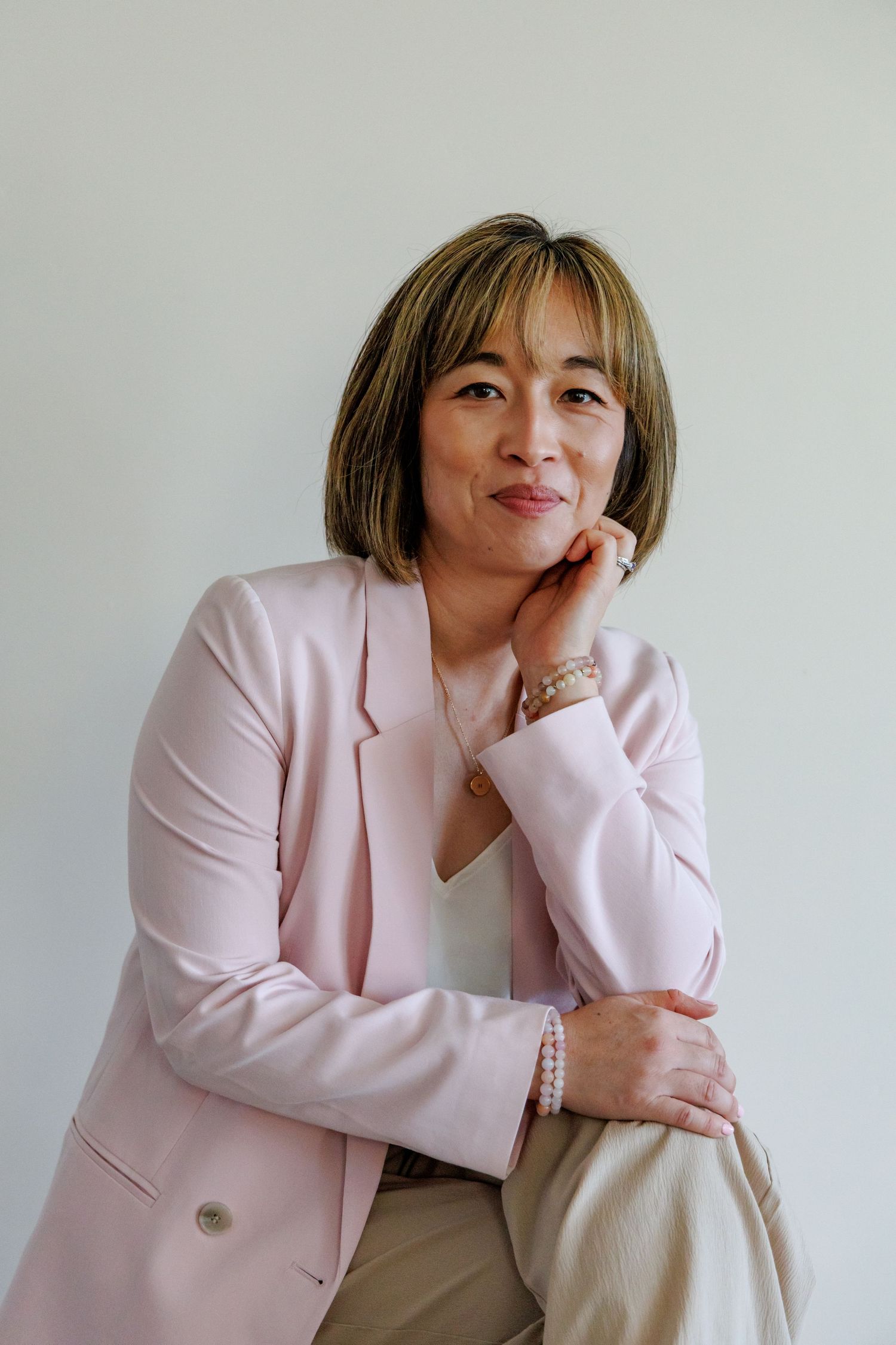 Elegant woman in pink blazer posing thoughtfully with hand on chin against white background.