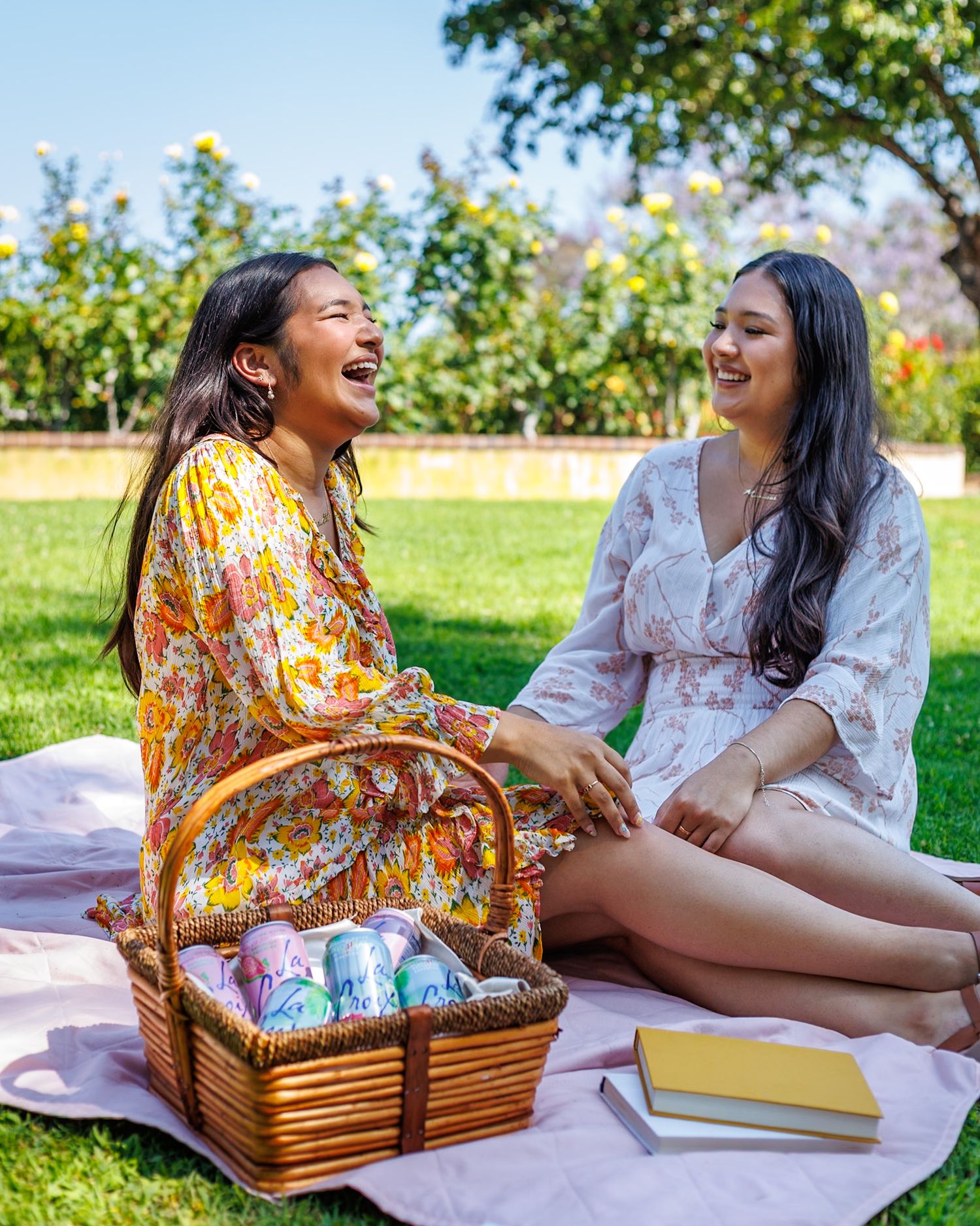 Two young women laughing together at a sunny outdoor picnic with a wicker basket of LaCroix drinks.