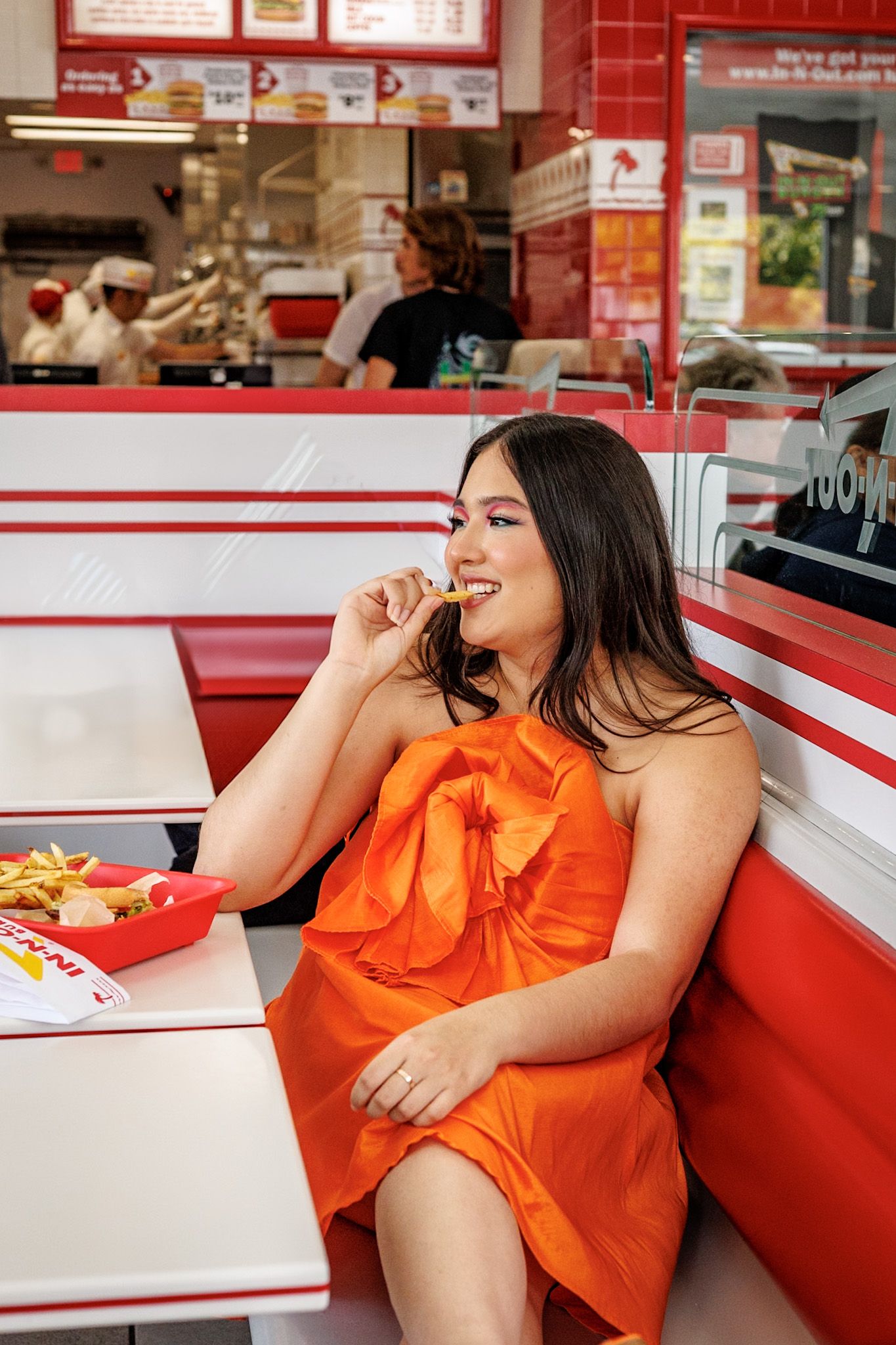 Woman in an orange dress eating french fries while sitting in an In-N-Out Burger booth.