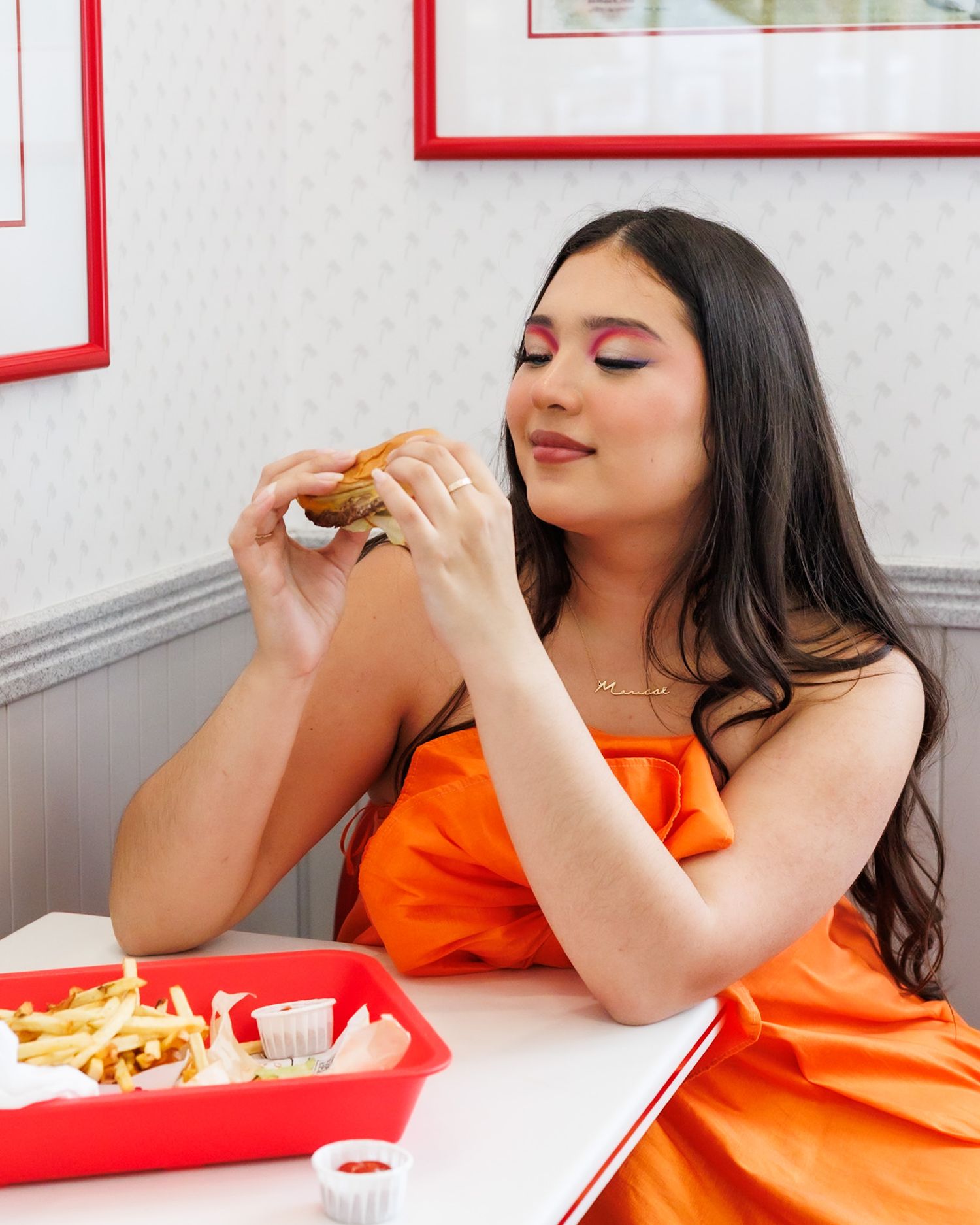 Woman in an orange dress eating a burger at an In-N-Out Burger restaurant booth.