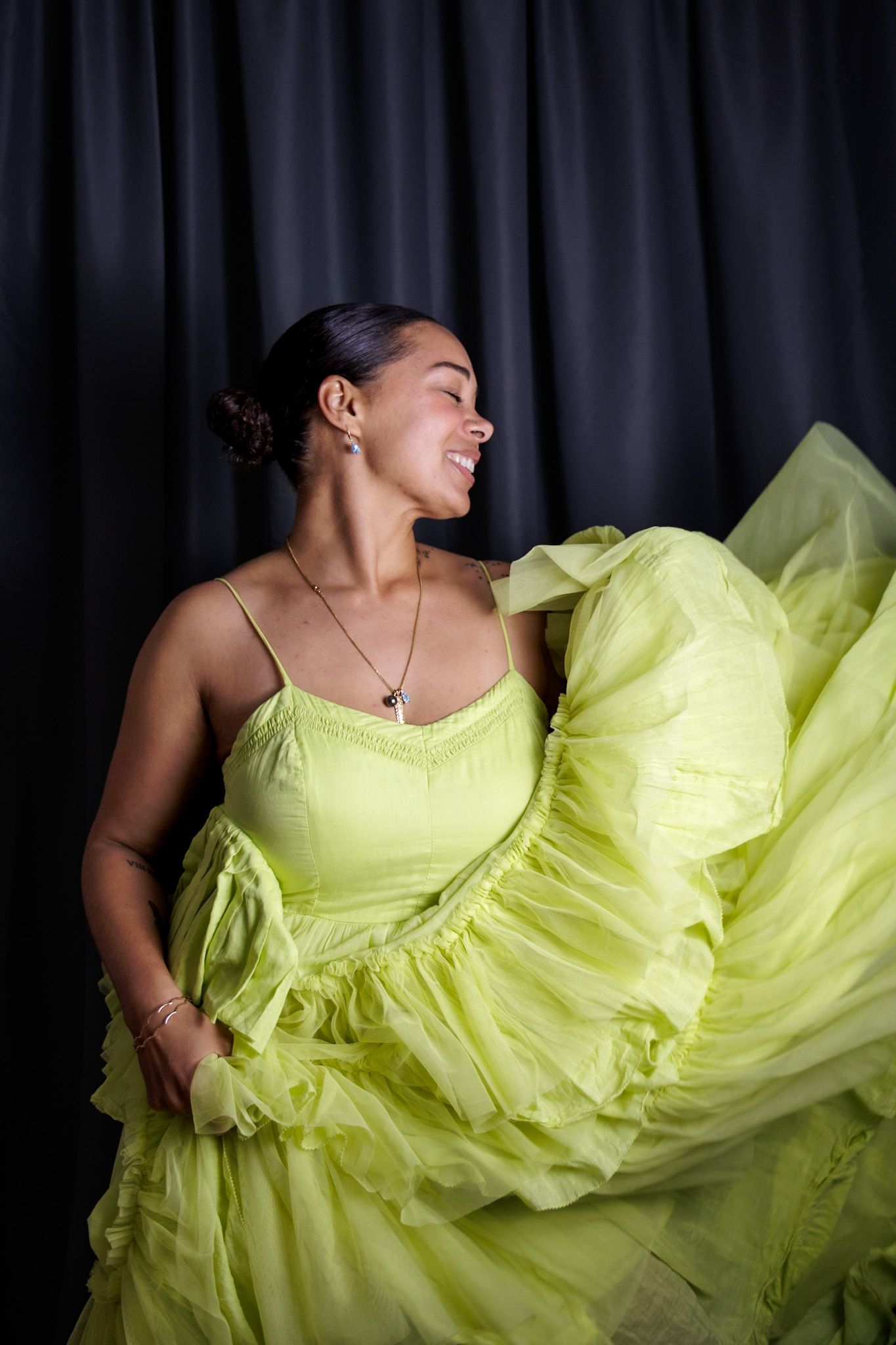Woman in voluminous lime green tulle gown twirling against dark curtain background.