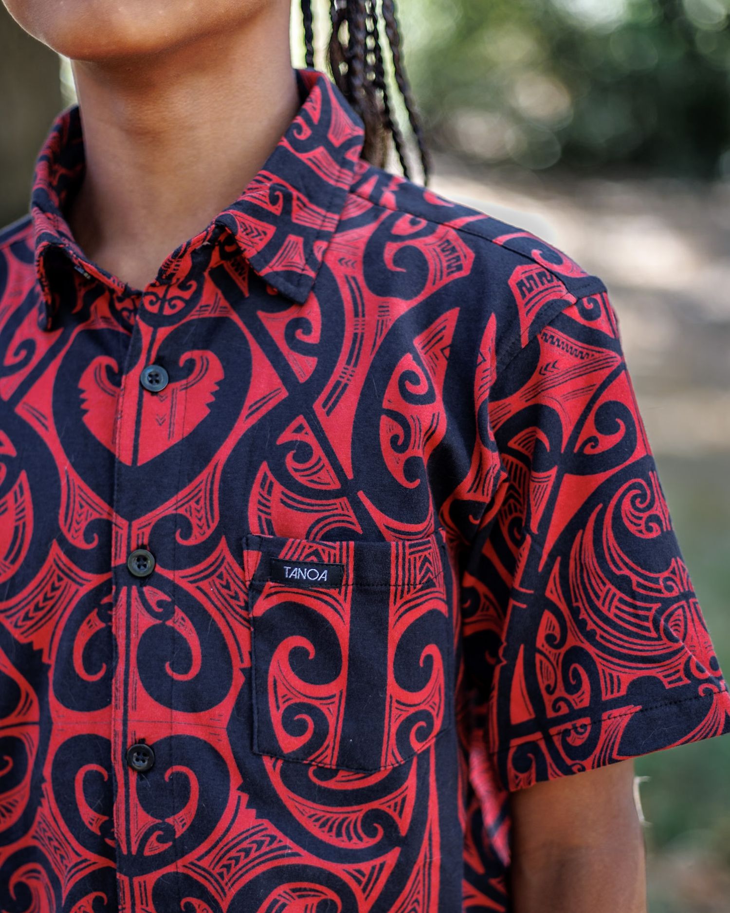 Close-up of a red and black Maori tribal print short-sleeve button-up shirt with a branded chest pocket.