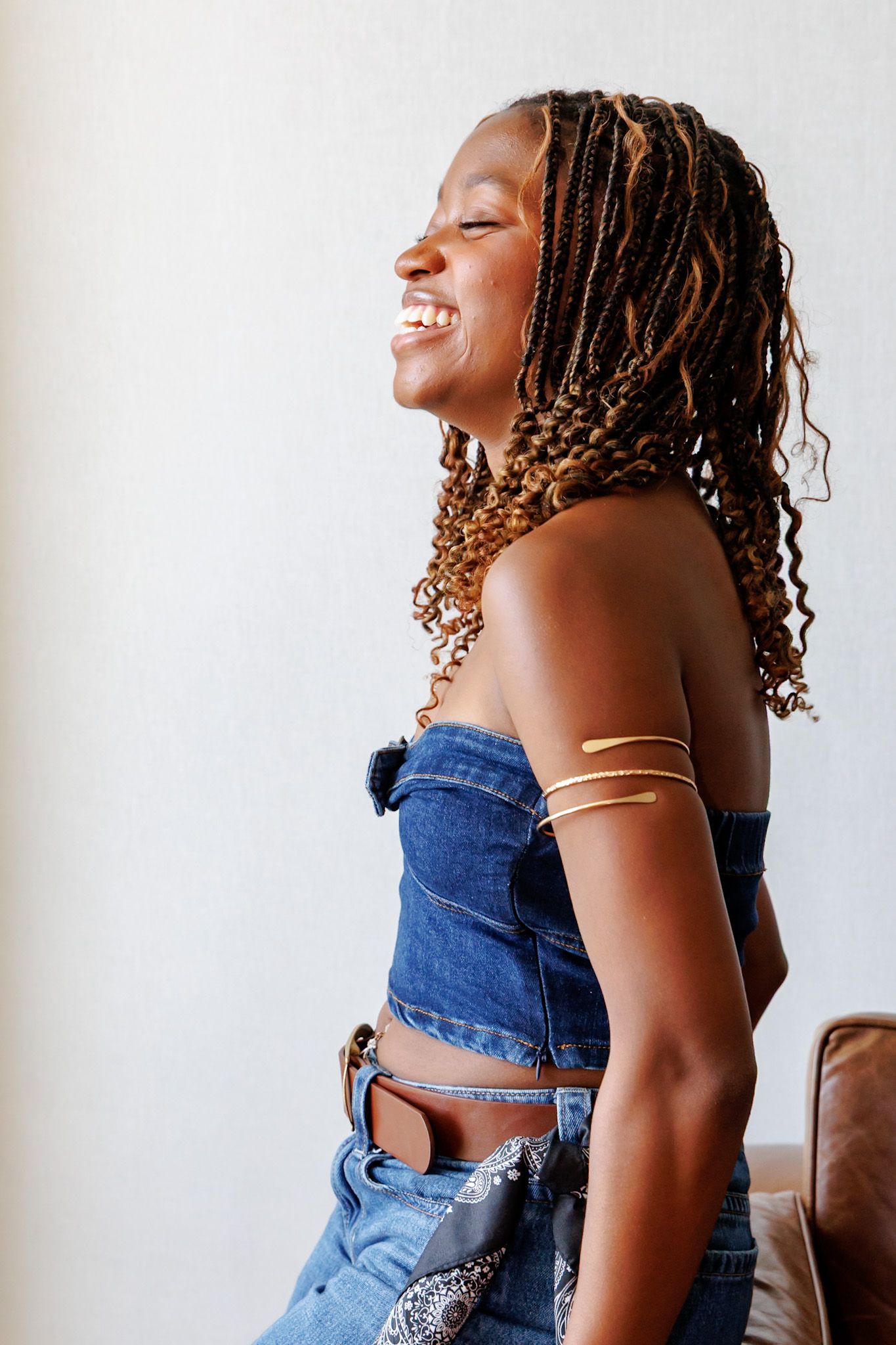 Joyful Black woman laughing in profile wearing denim strapless top with gold arm cuff and paisley bandana.