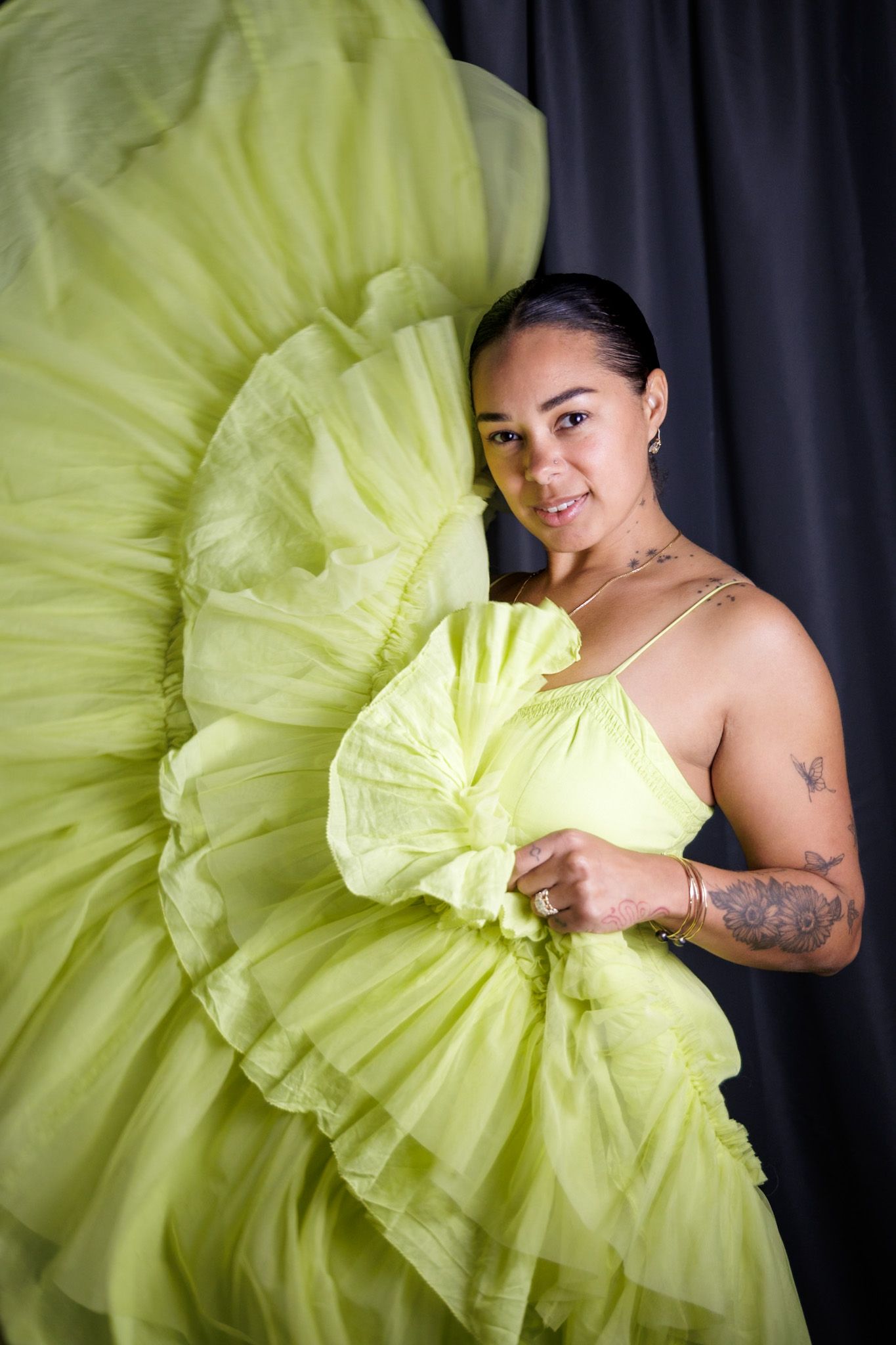Woman in flowing lime green tulle gown posing with ruffled fabric against dark backdrop.