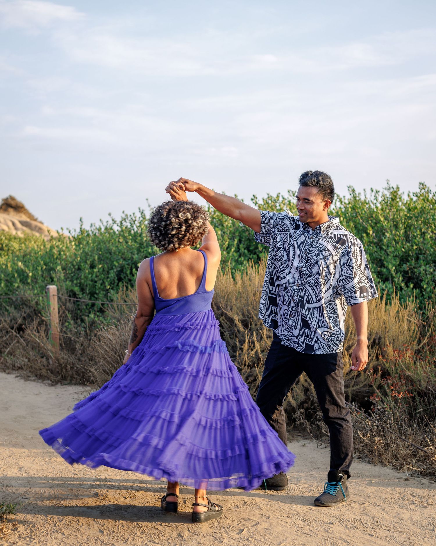 Couple dances on a scenic outdoor path surrounded by lush greenery at golden hour.