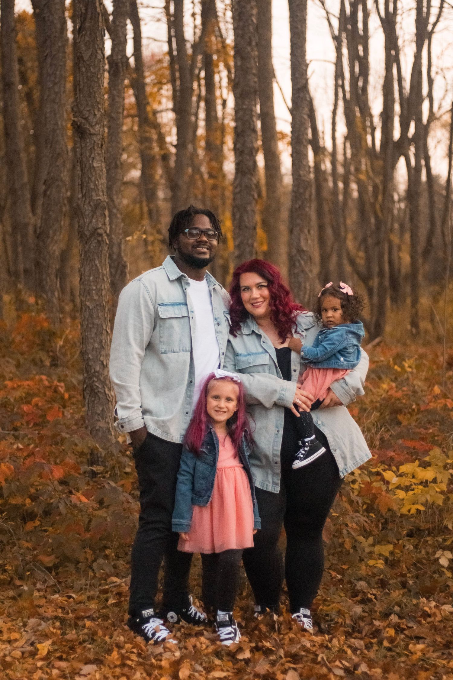 Family of four in matching denim jackets posing in autumn forest at sunset.