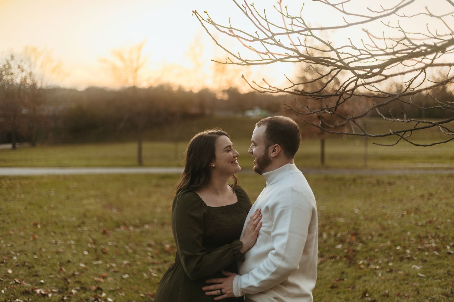 Couple laughing together in park at golden hour near bare trees.