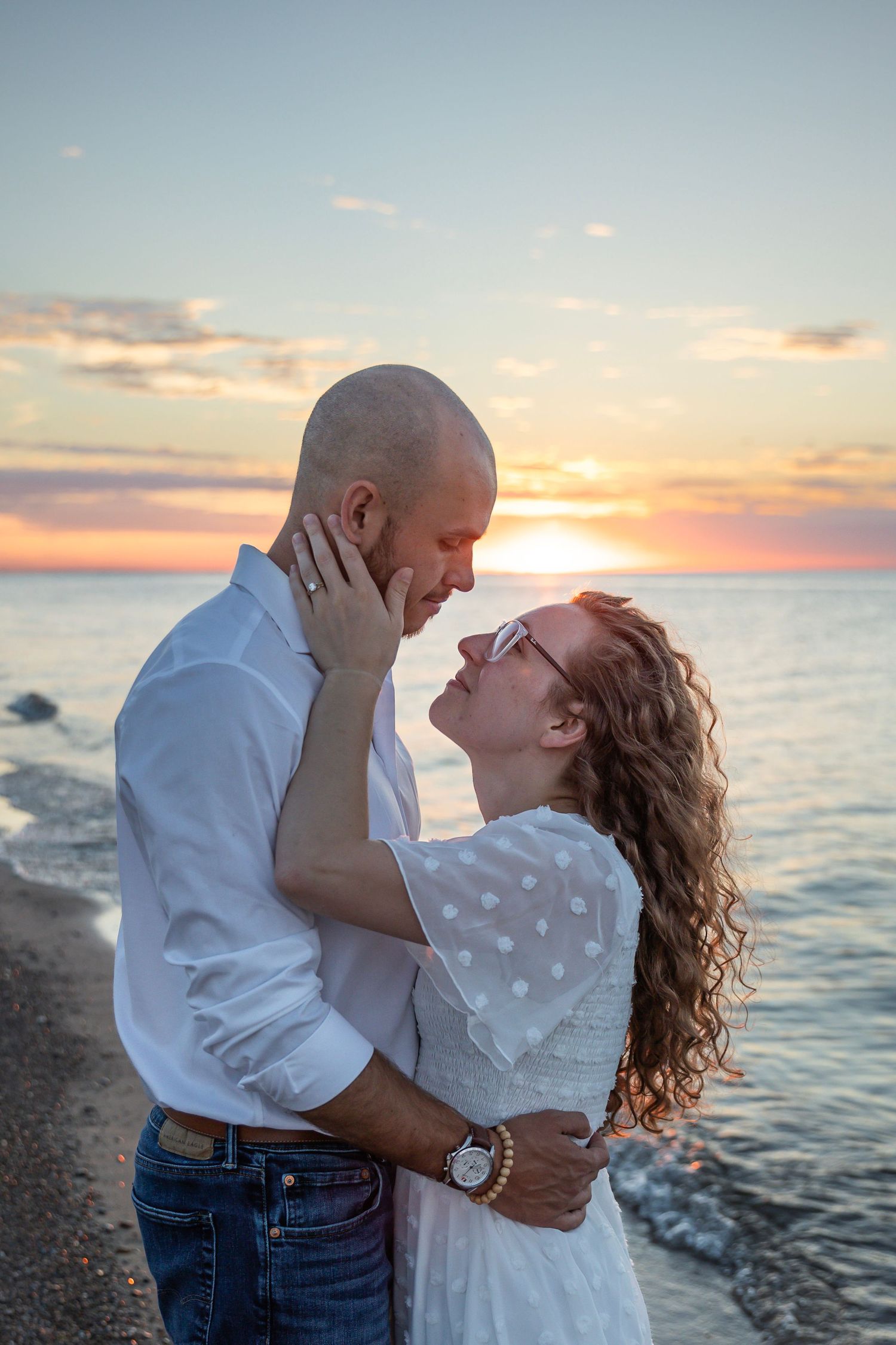 Engaged couple embracing along a Lake Michigan beach in Indiana during a natural, candid engagement session.