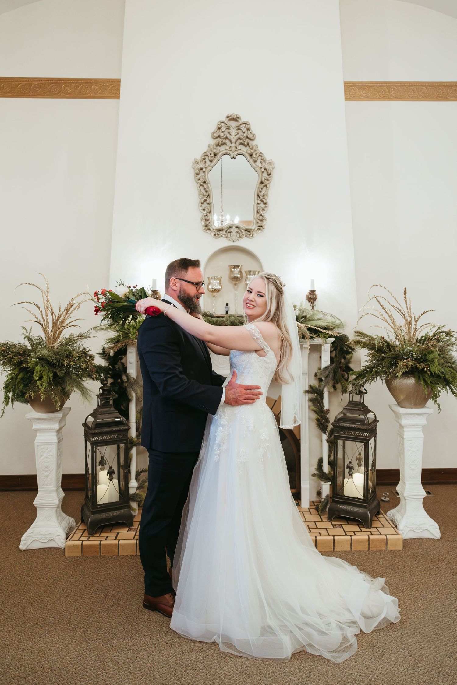 Indoor winter wedding portrait in Michigan featuring bride and groom smiling together near a decorated fireplace