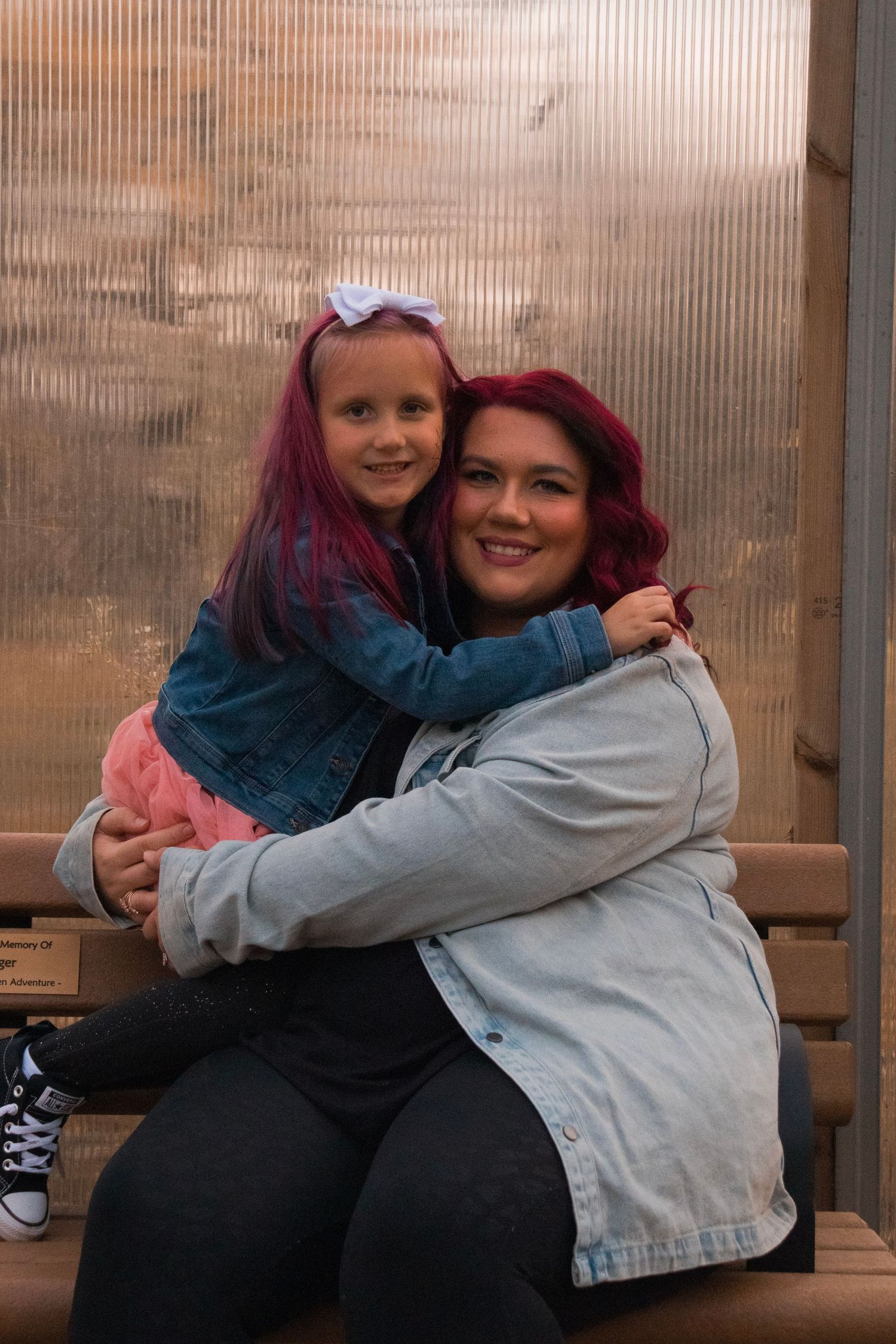 Mother and daughter with matching red hair hugging warmly on a wooden bench.
