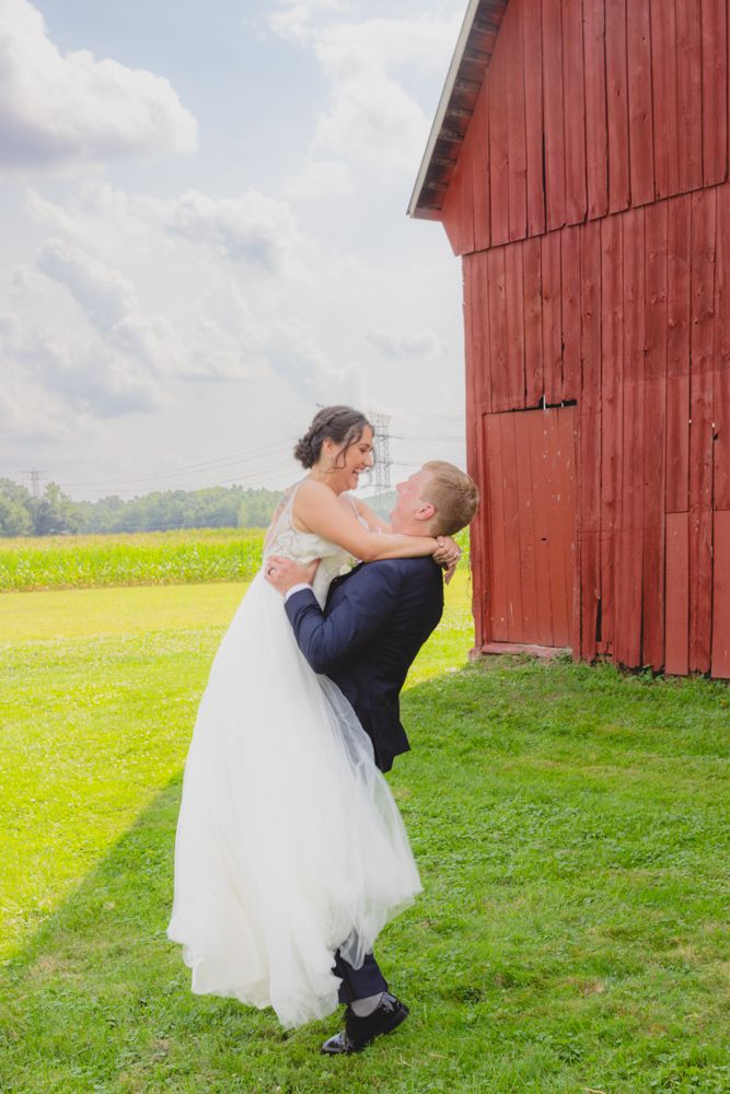 Bride and groom portrait at an August wedding in New Boston, Michigan standing together in front of a rustic red barn