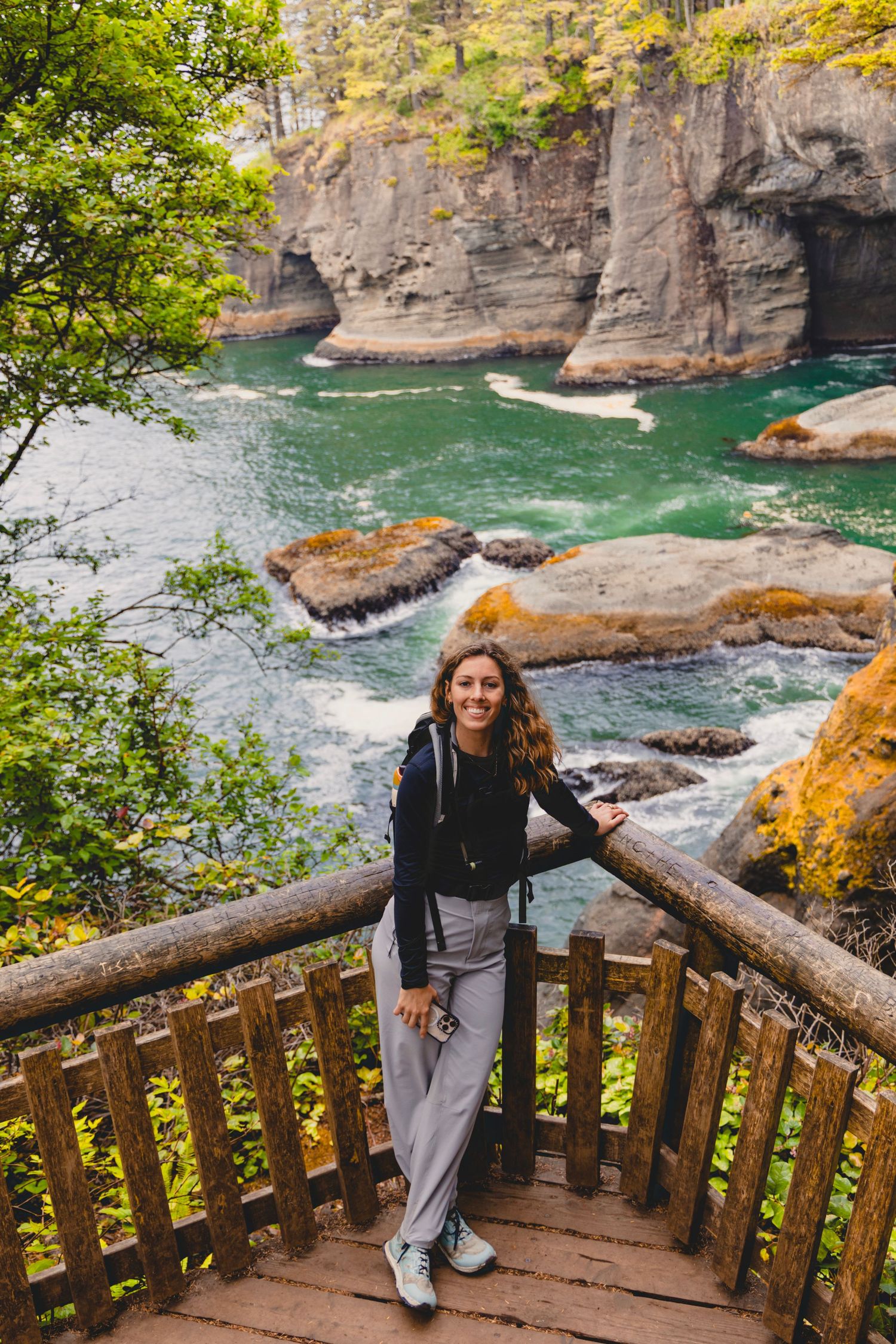 Woman standing at a scenic overlook above turquoise water and rocky cliffs in Olympic national park