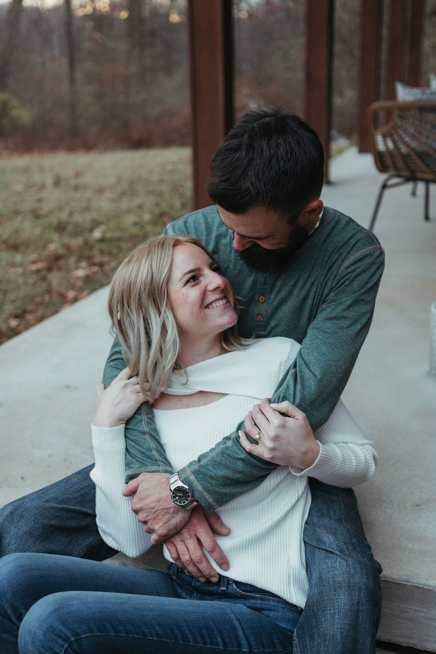 Cozy winter engagement session in Lapeer, Michigan with a couple standing together on a porch in soft natural light