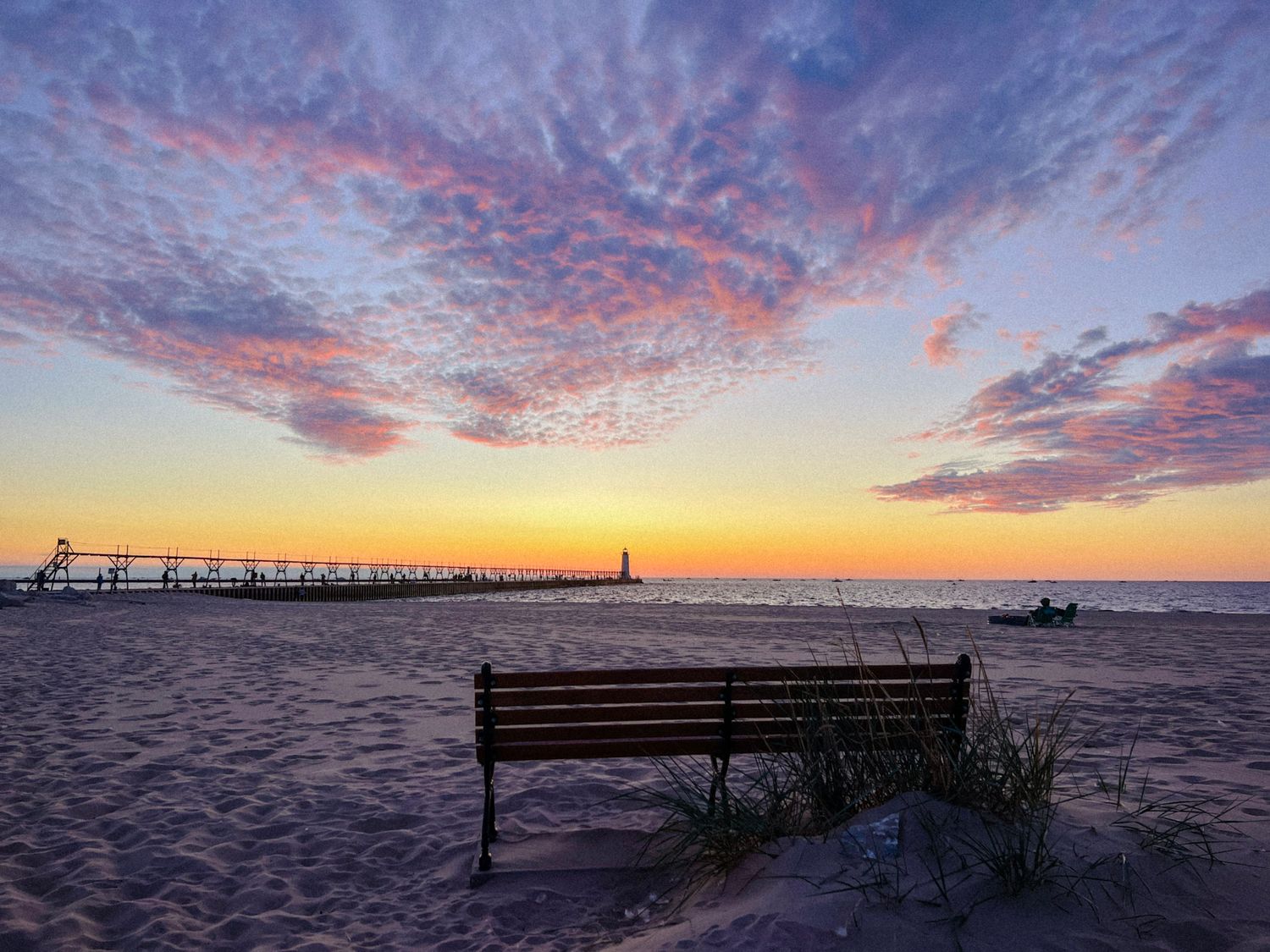 Sunset over Lake Michigan in Manistee with a park bench overlooking the beach and calm water