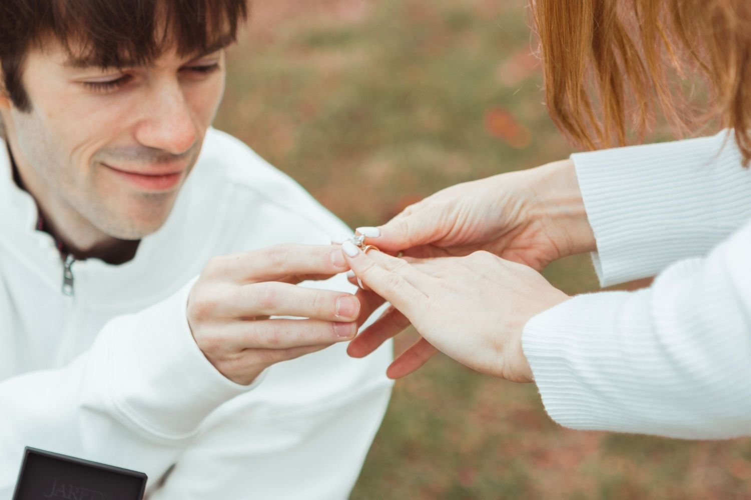 Candid fall engagement photo in Oakland County, Michigan capturing the groom-to-be placing the engagement ring on her finger