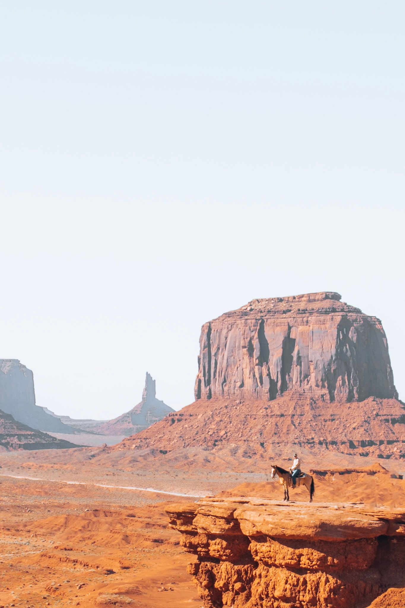 Person riding a horse at John Wayne Point in Monument Valley with red rock buttes in the background