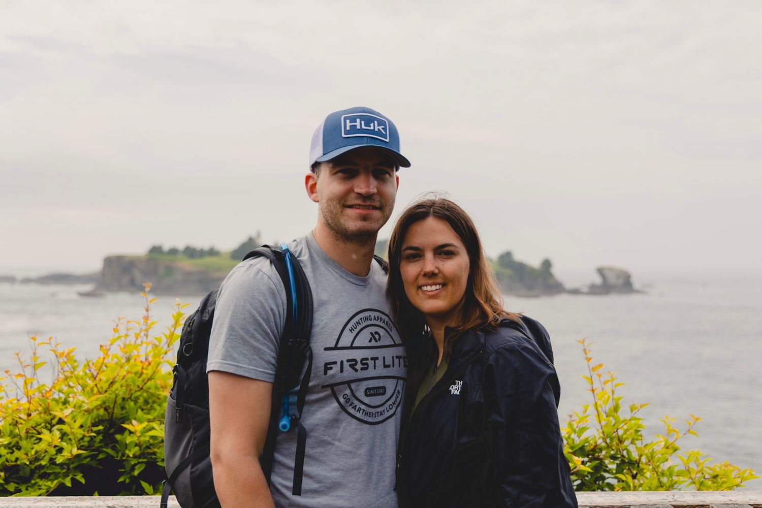 Smiling couple posing together with ocean island backdrop on cloudy day outdoor adventure.
