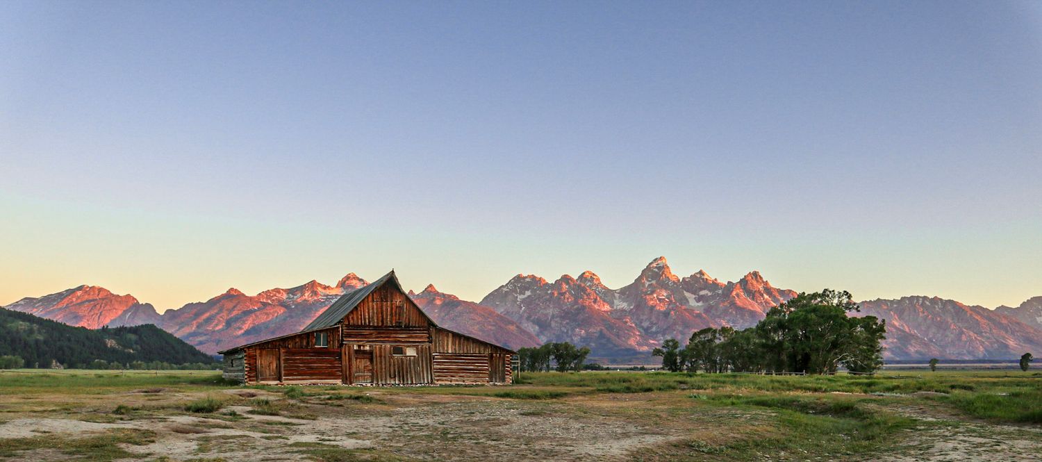 Historic Mormon Row barn at sunrise with the Teton Range glowing pink in Grand Teton National Park.
