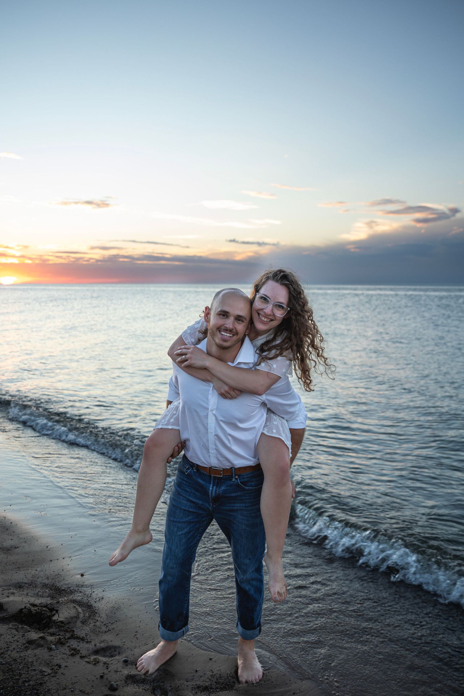 Engaged couple embracing along a Lake Michigan beach in Indiana during a natural, candid engagement session.