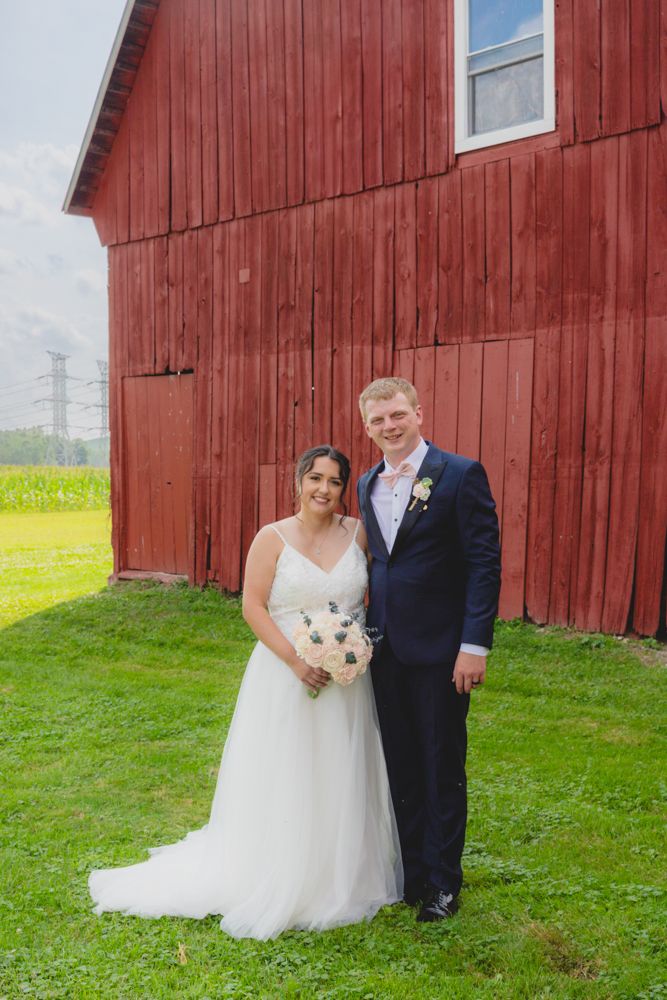 Bride and groom portrait at an August wedding in New Boston, Michigan standing together in front of a rustic red barn