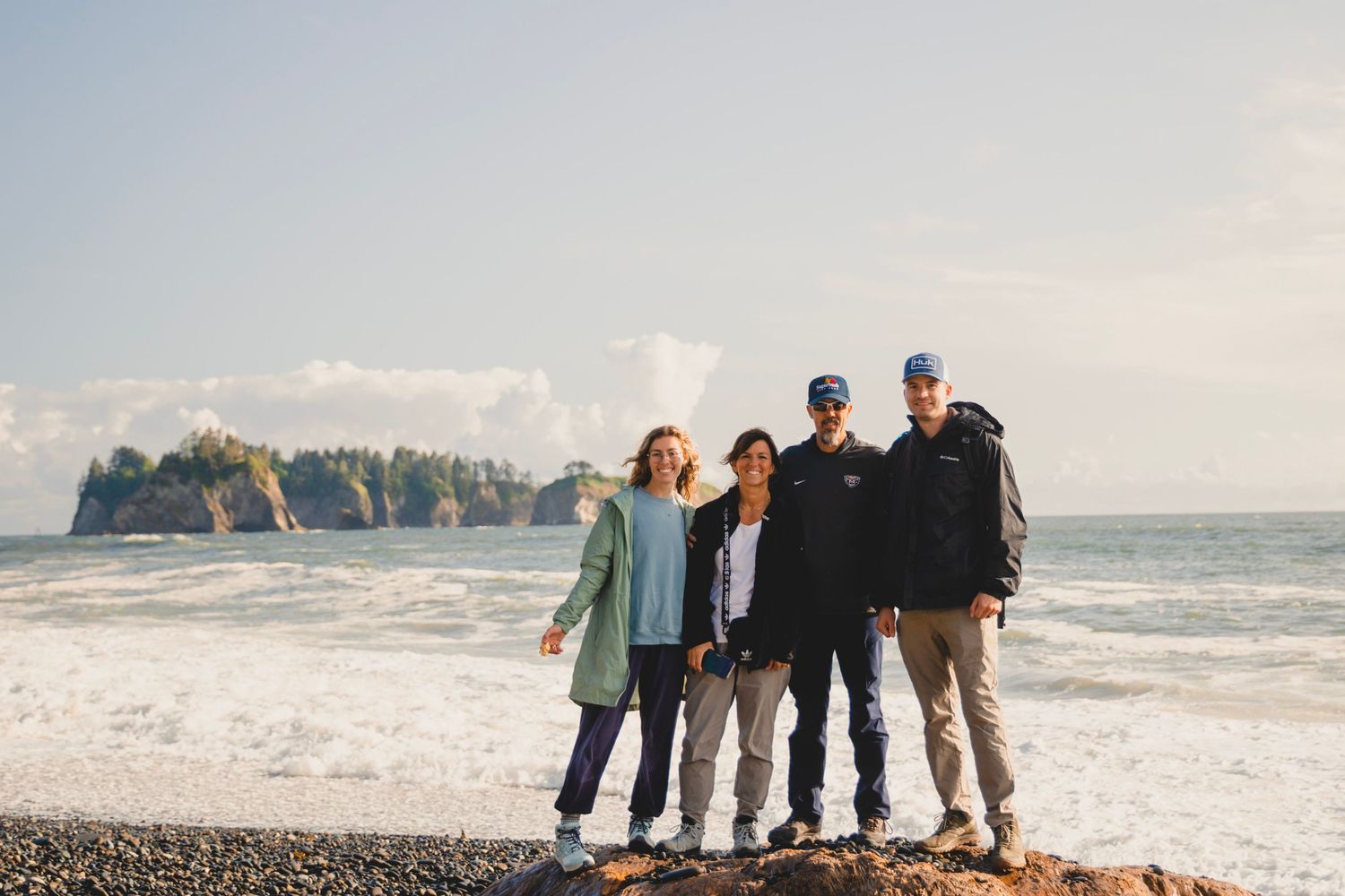 Group standing on the rocky shore at Rialto Beach in Olympic National Park with ocean waves and sea stacks behind them