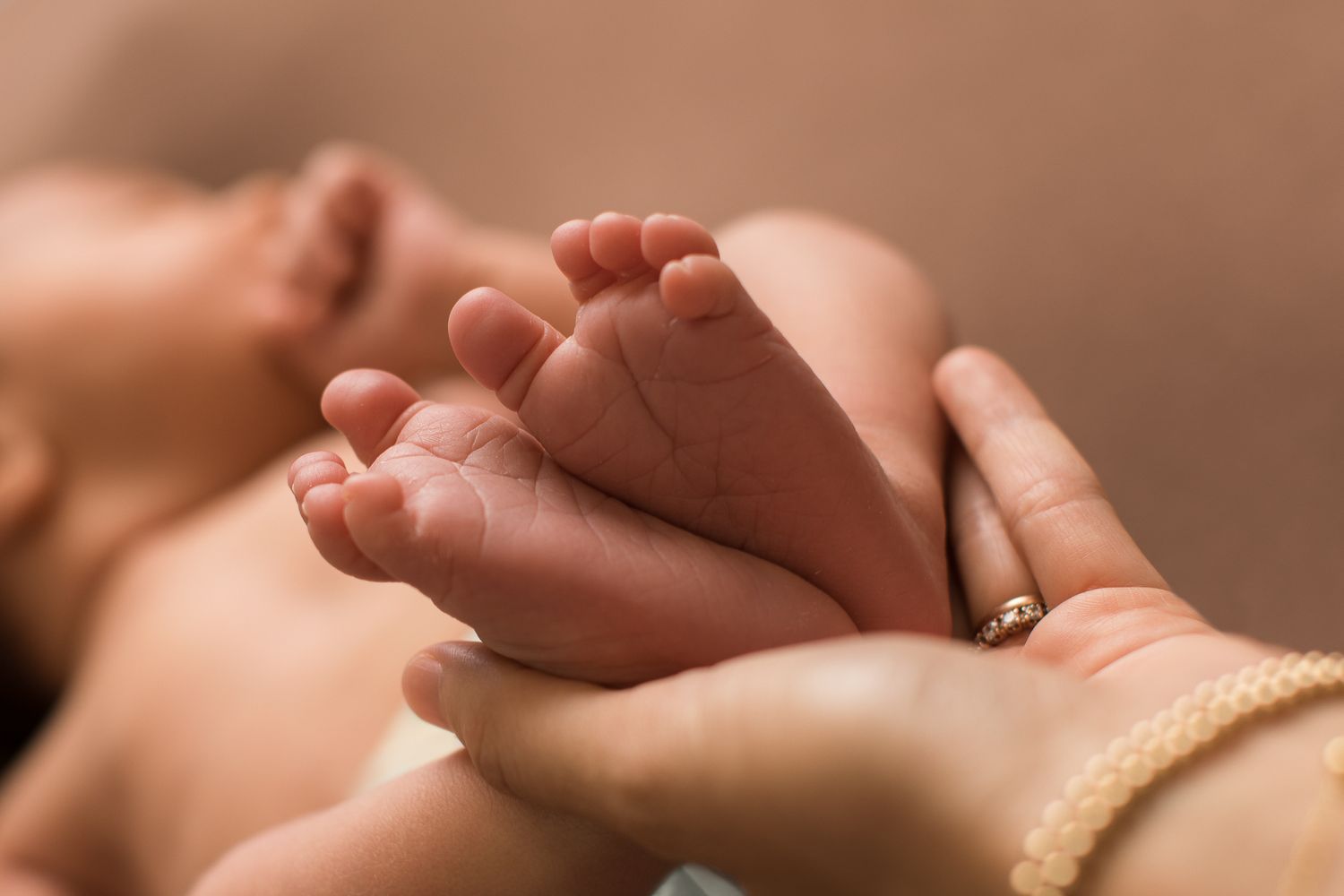 Adult hands gently cradling tiny newborn baby feet, capturing a tender moment of new parenthood.