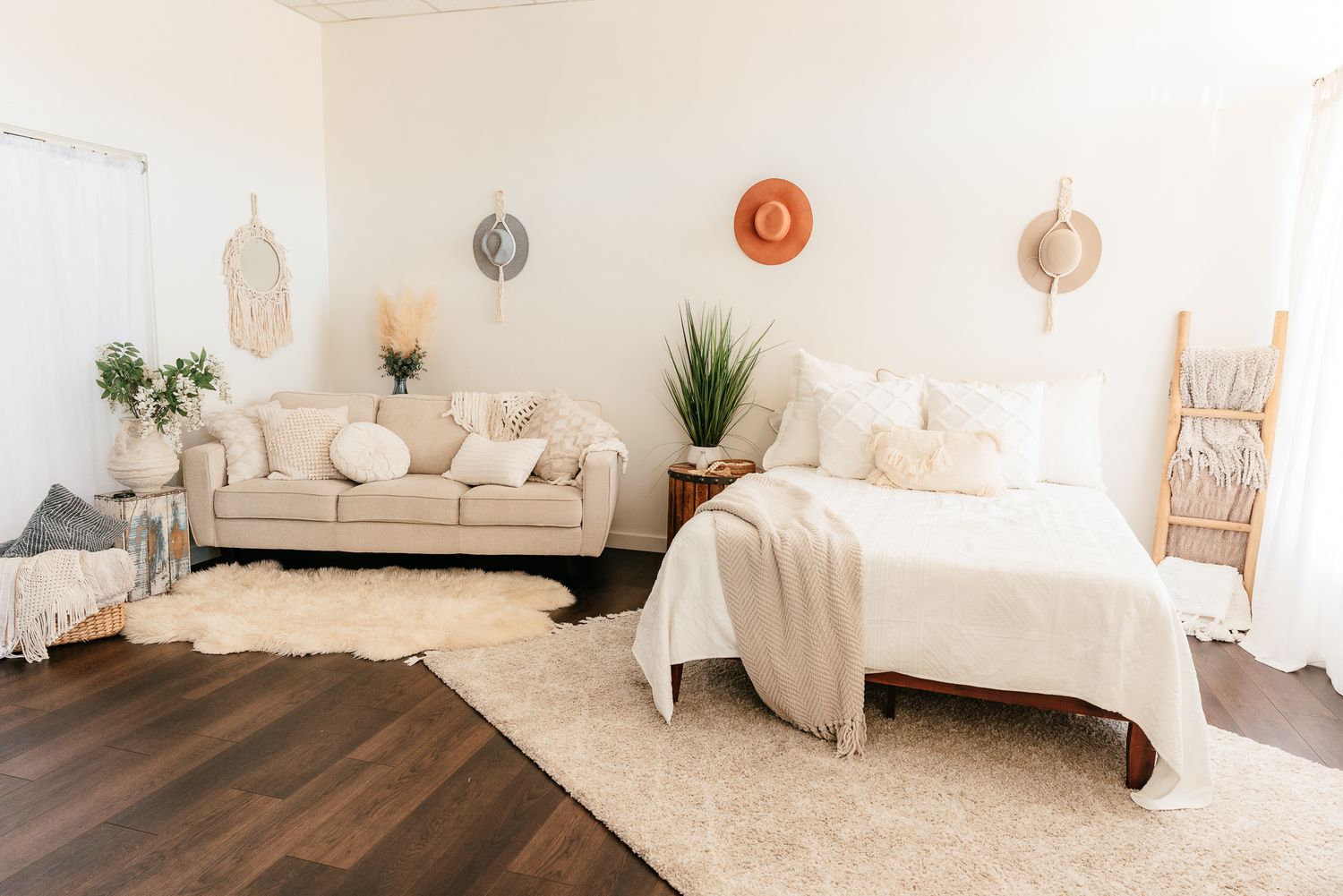 Bohemian bedroom with cream sofa, white bed, layered rugs, woven wall hangings, and potted plants. in the Bonsall Studio near Fallbrook, Vis