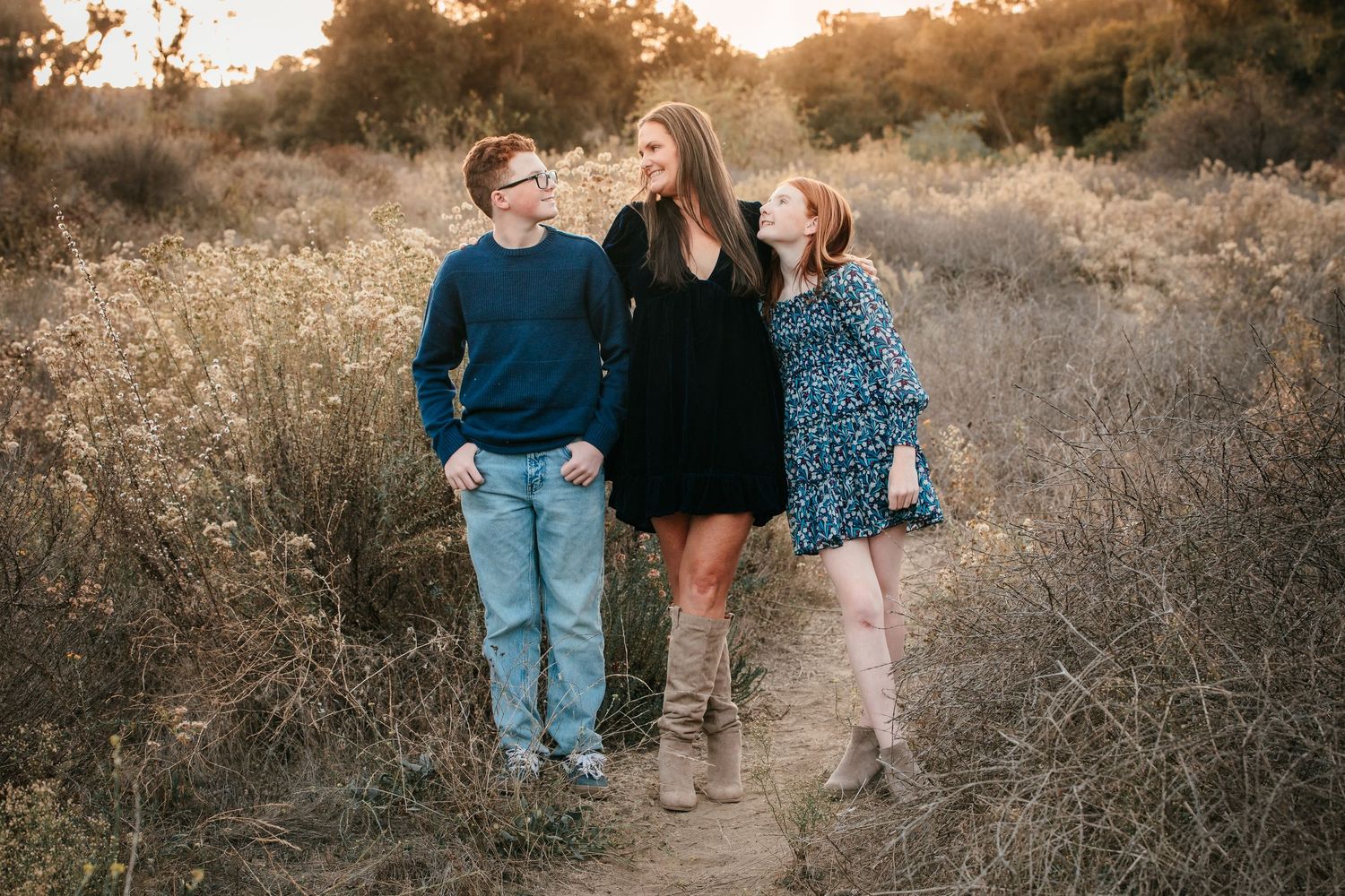 Mother walking with teenage son and daughter along a nature trail during golden hour.