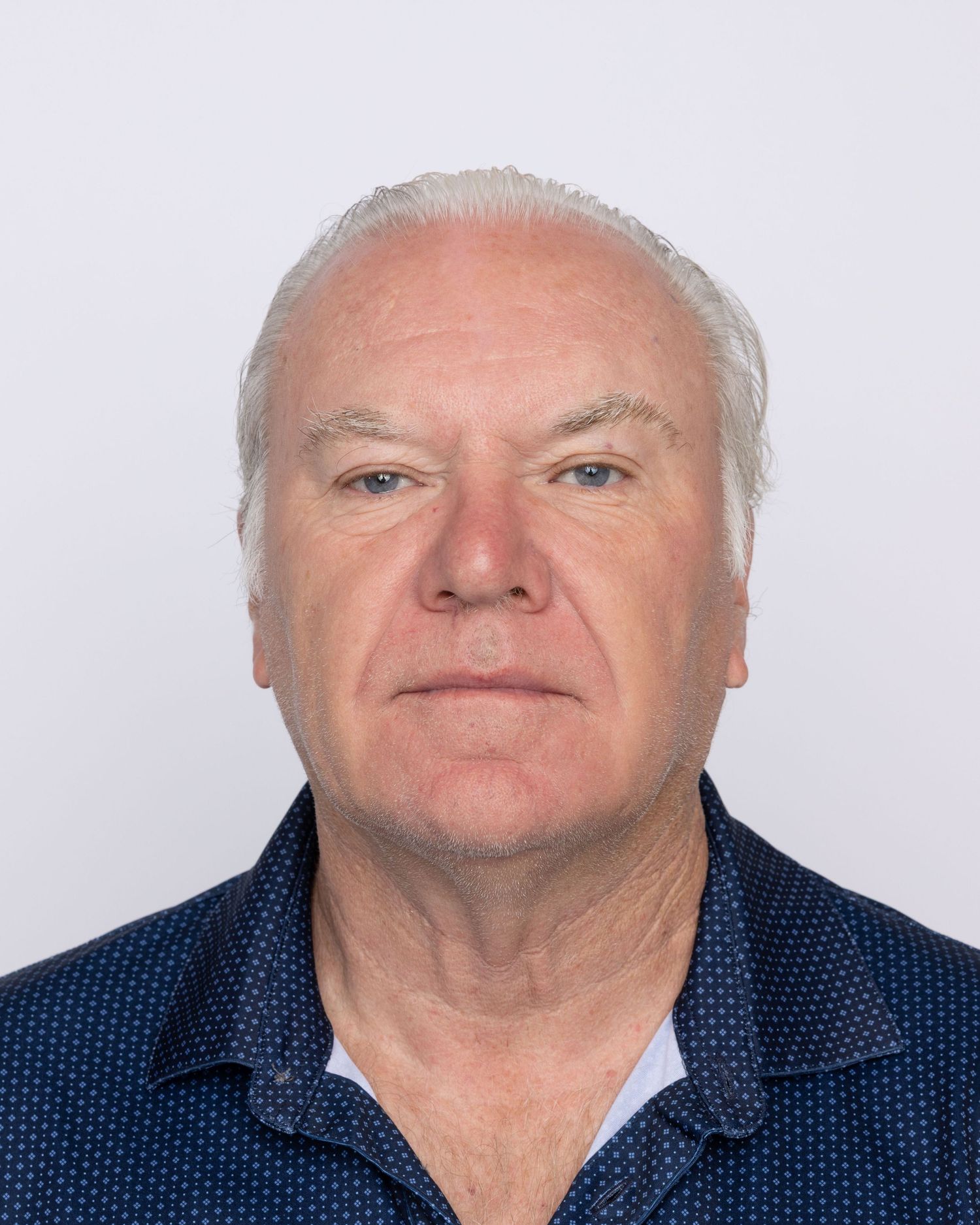 Older man with short white hair wearing a navy blue patterned shirt, posing for a professional headshot photo.