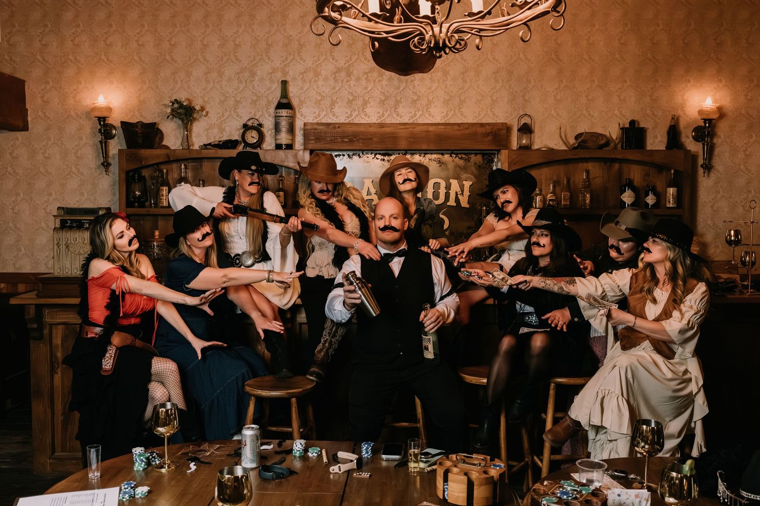 Wild West themed group photo with costumed guests celebrating around a rustic saloon bar with dramatic poses.